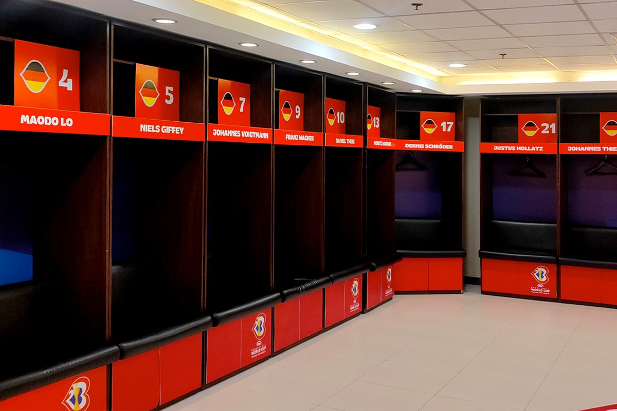 Empty locker stalls in a football team's locker room with Dutch flags and player names displayed above each stall.