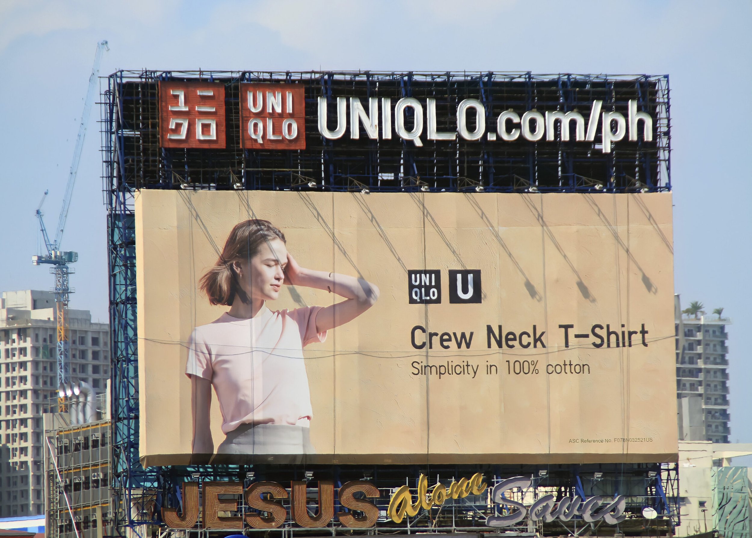 Billboard for UNIQLO featuring a woman in a pink shirt and gray skirt, with text about crew neck T-shirts made of 100% cotton, and the UNIQLO logo.