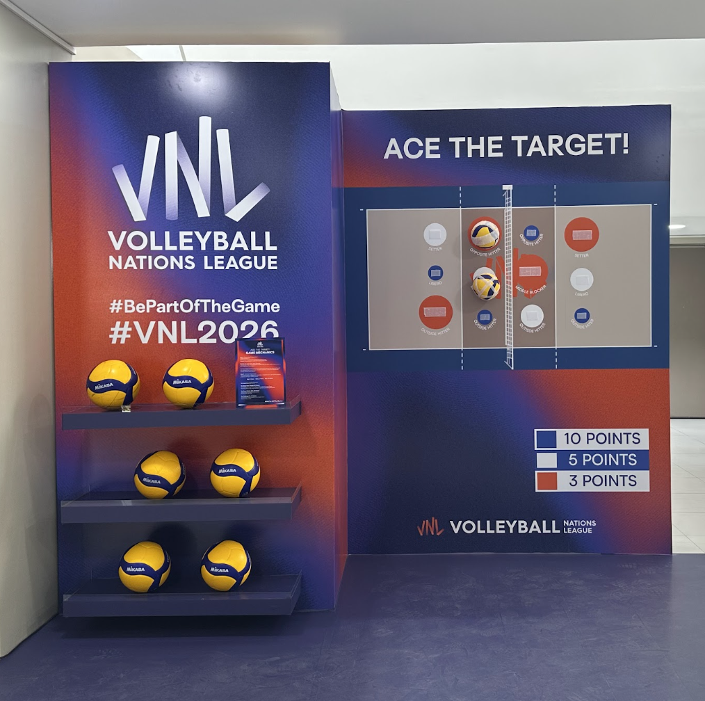 A volleyball-themed interactive game display featuring a large poster about the Volleyball Nations League (VNL) 2026, with volleyballs on shelves, and a court diagram with scoring zones for a game called "Ace the Target!"