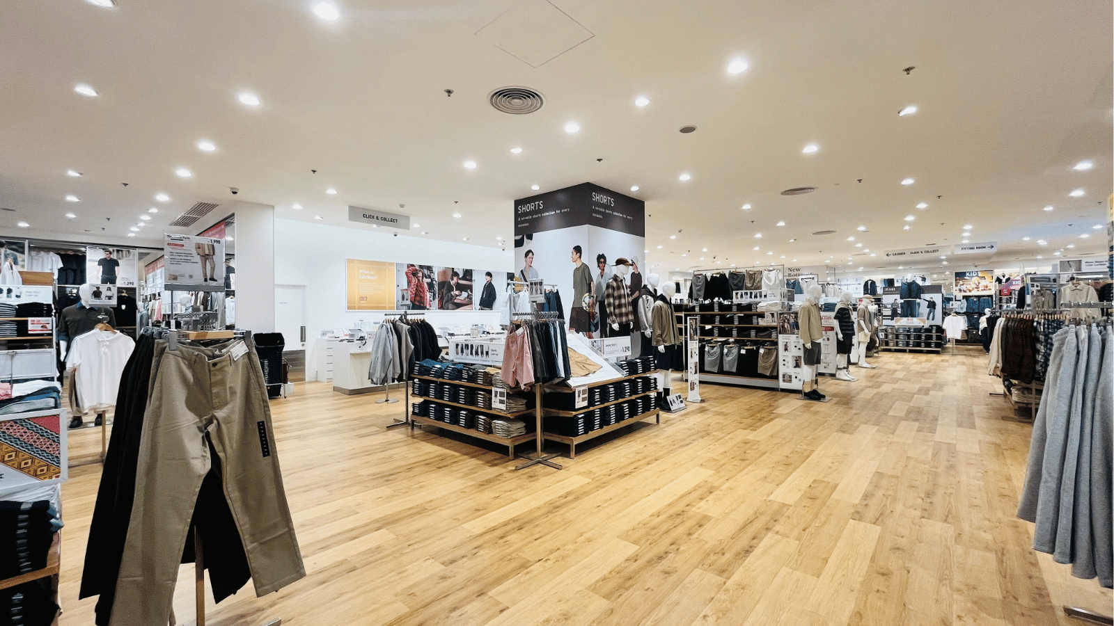Interior of a UNIQLO store with various racks and mannequins displaying casual clothing, wooden floors, and bright overhead lighting.