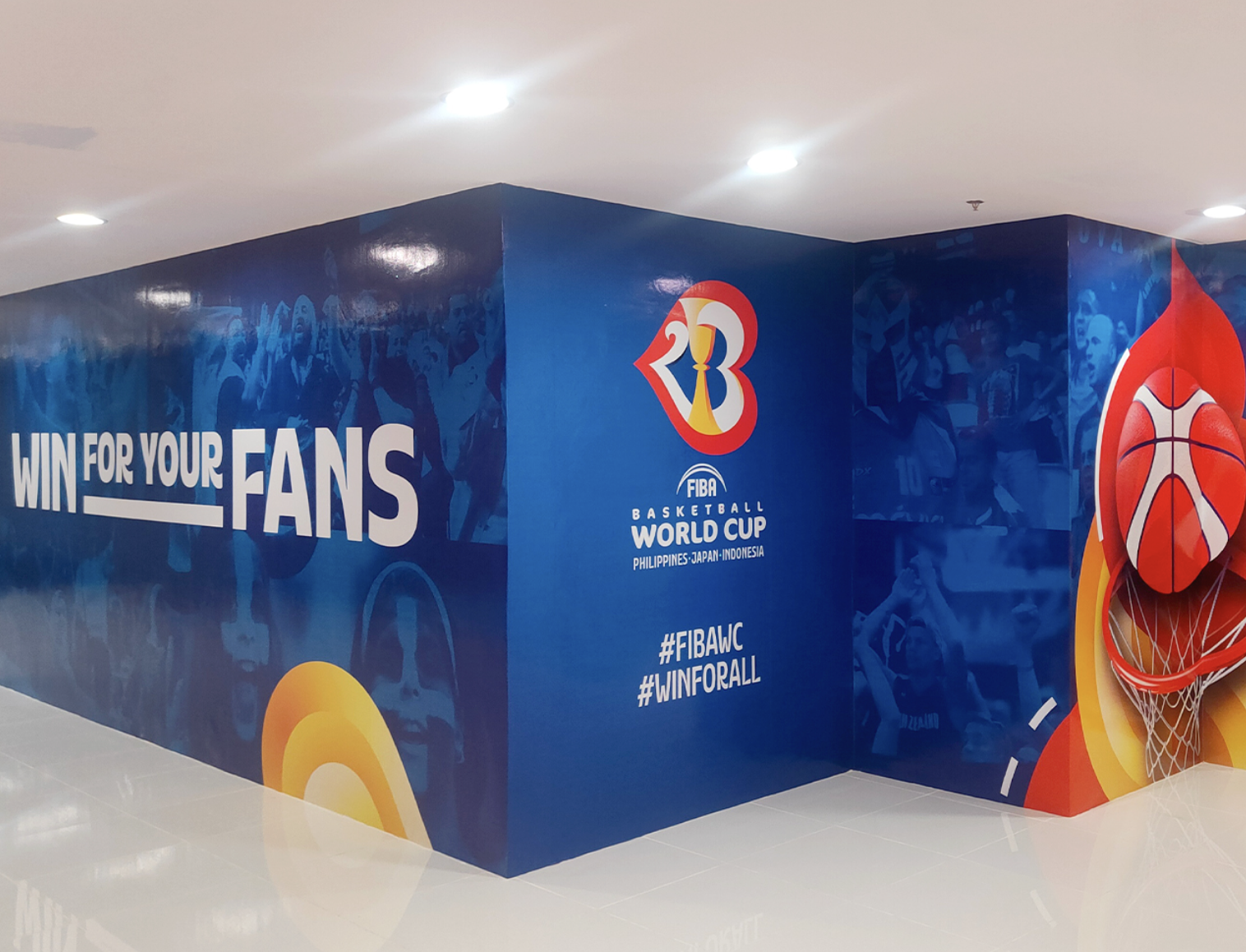 Wall mural promoting the FIBA Basketball World Cup with the slogan "Win for your fans" on the left, the event logo in the center, and a basketball hoop with a basketball on the right.