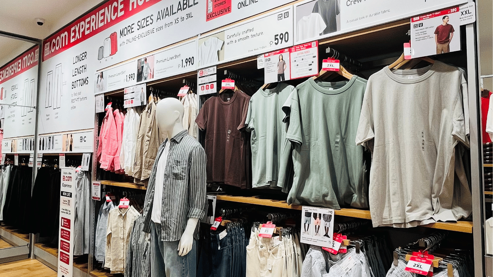 UNIQLO store display with men's and women's casual wear, including T-shirts, shirts, and pants, arranged on shelves and hangers.