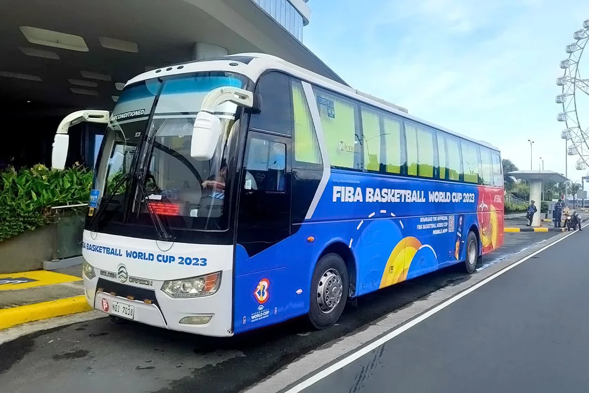 A bus parked at a curb with a FIBA Basketball World Cup 2023 advertisement on its side, featuring vibrant colors and graphics related to the basketball event.