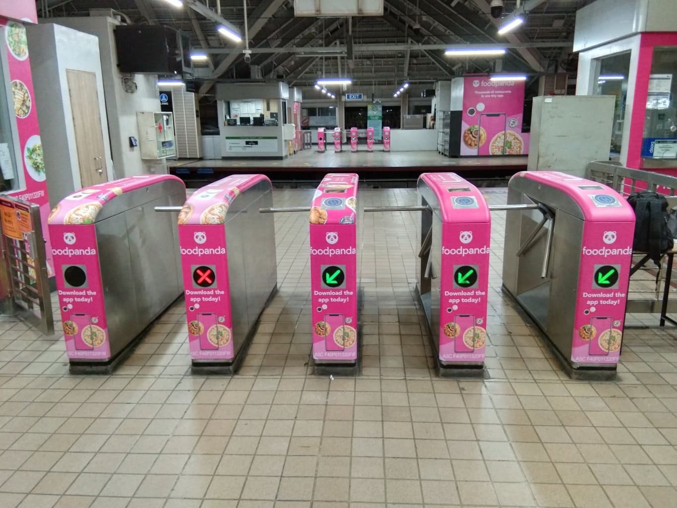 Entrance gate at Foodpanda delivery pickup area, with pink branding and electronic scanning pads, in a well-lit indoor location, possibly a train station or mall.