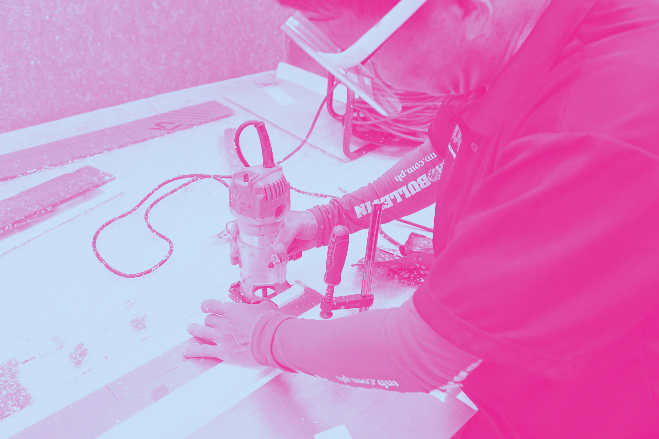 Person operating a power tool on flooring during construction, with pink overlay.