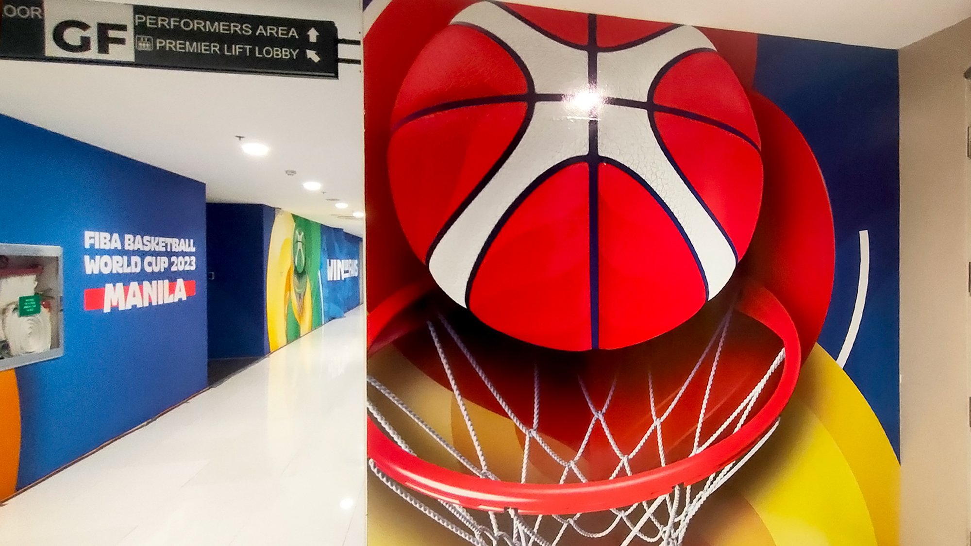A large three-dimensional basketball hoop and backboard decoration in a hallway, with text mentioning the FIBA Basketball World Cup 2023 in Manila.
