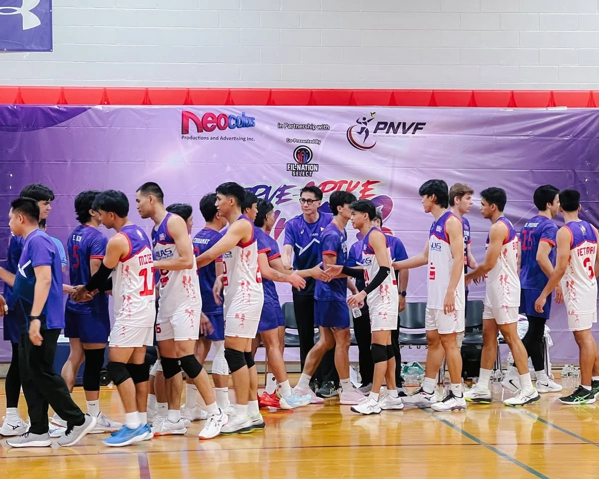 Youth male volleyball players in team uniforms shaking hands in a sports court.