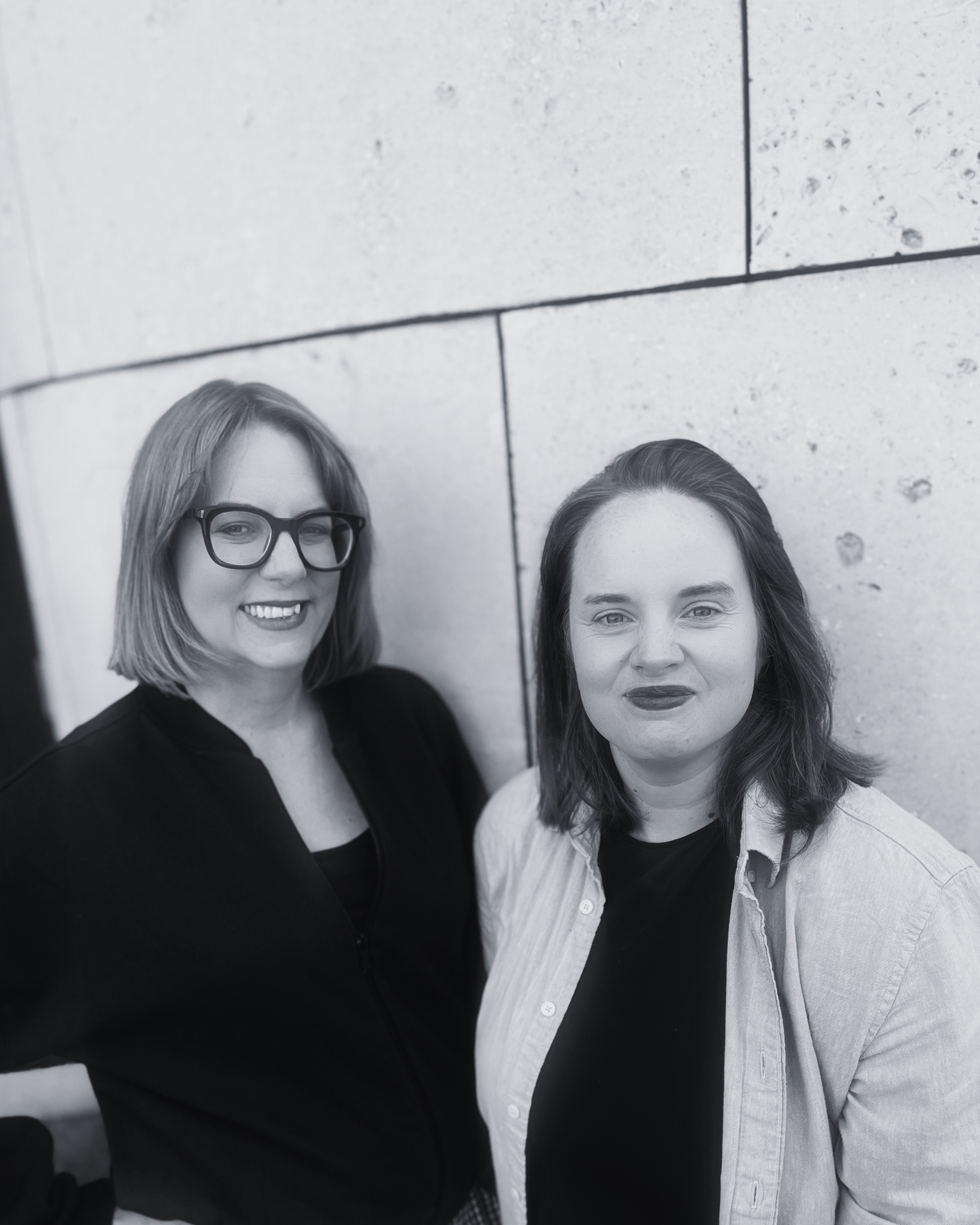 Black and white photograph showing two women standing next to each other smiling into the camera.