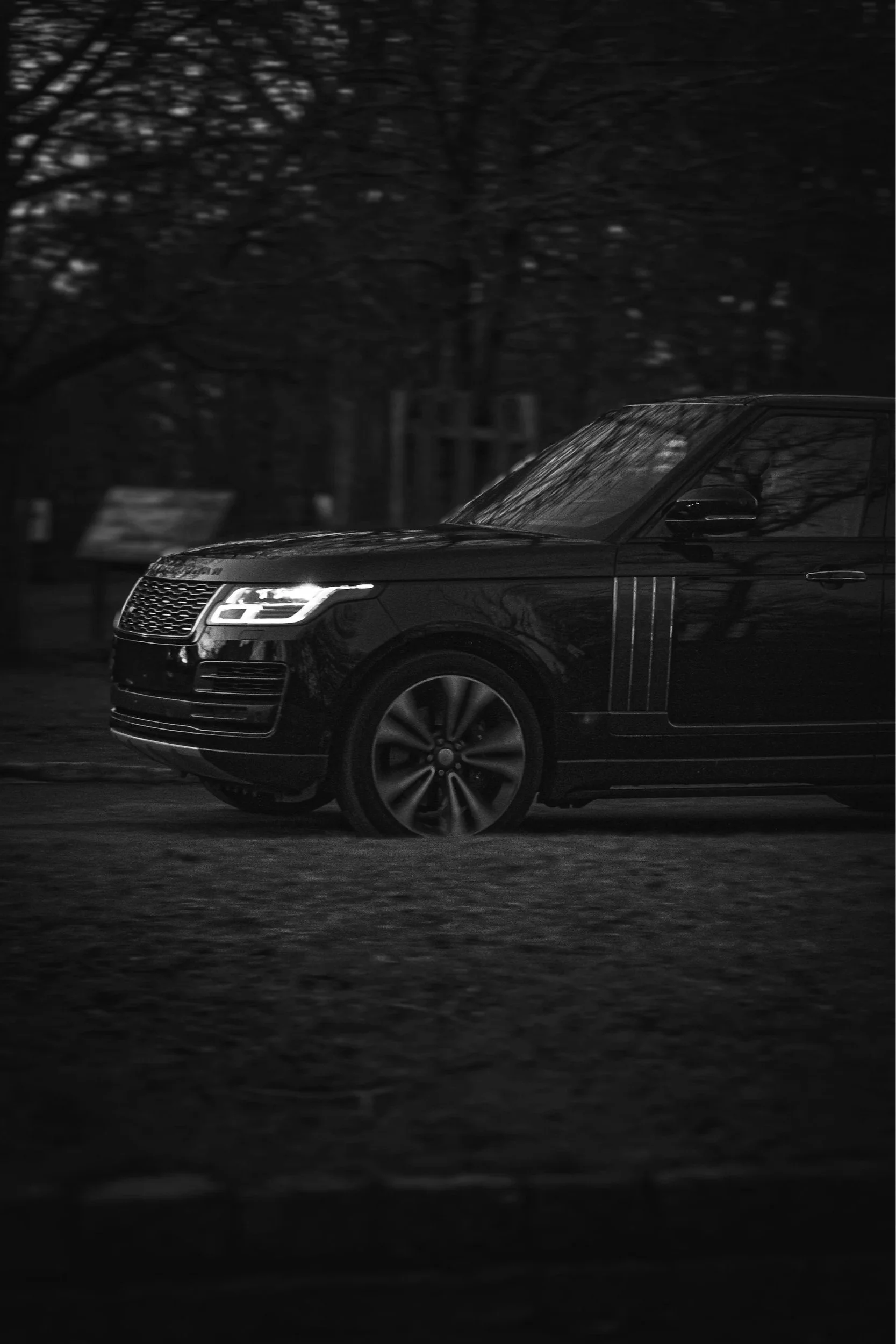 A black luxury SUV driving on a dark road at night with trees in the background.