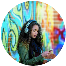 Young woman with headphones using her phone near colorful graffiti wall.