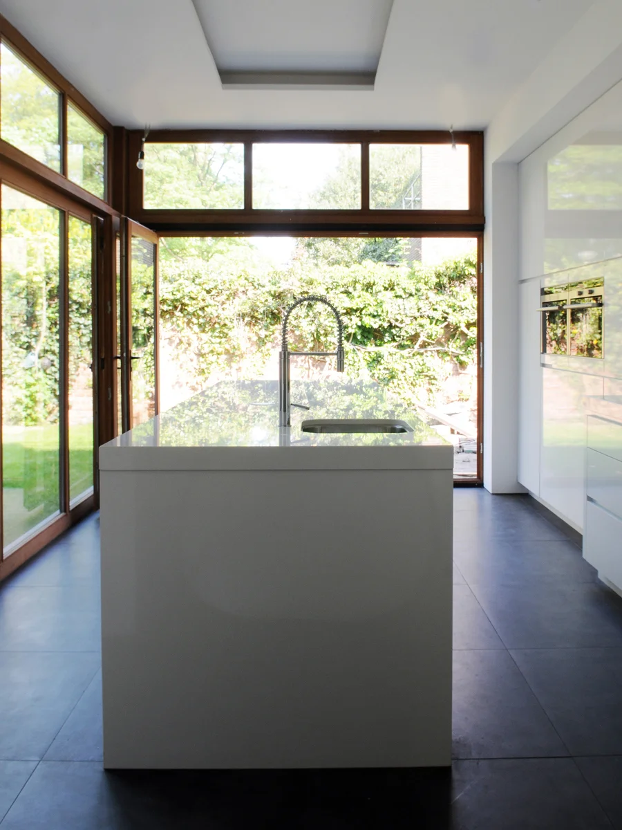 Modern kitchen with white island, black faucet, large windows, and sliding glass doors.