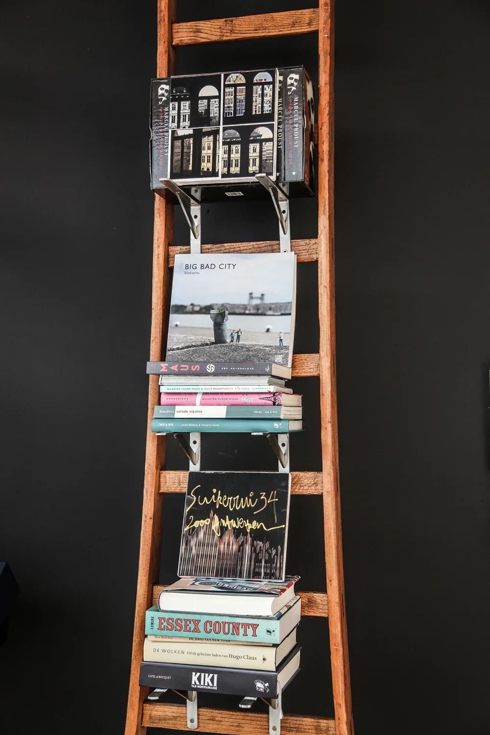 Bespoke wooden library ladder used as a creative book display against a dark accent wall, showcasing contemporary residential interior styling, by Tom Naeyaert Architecture.