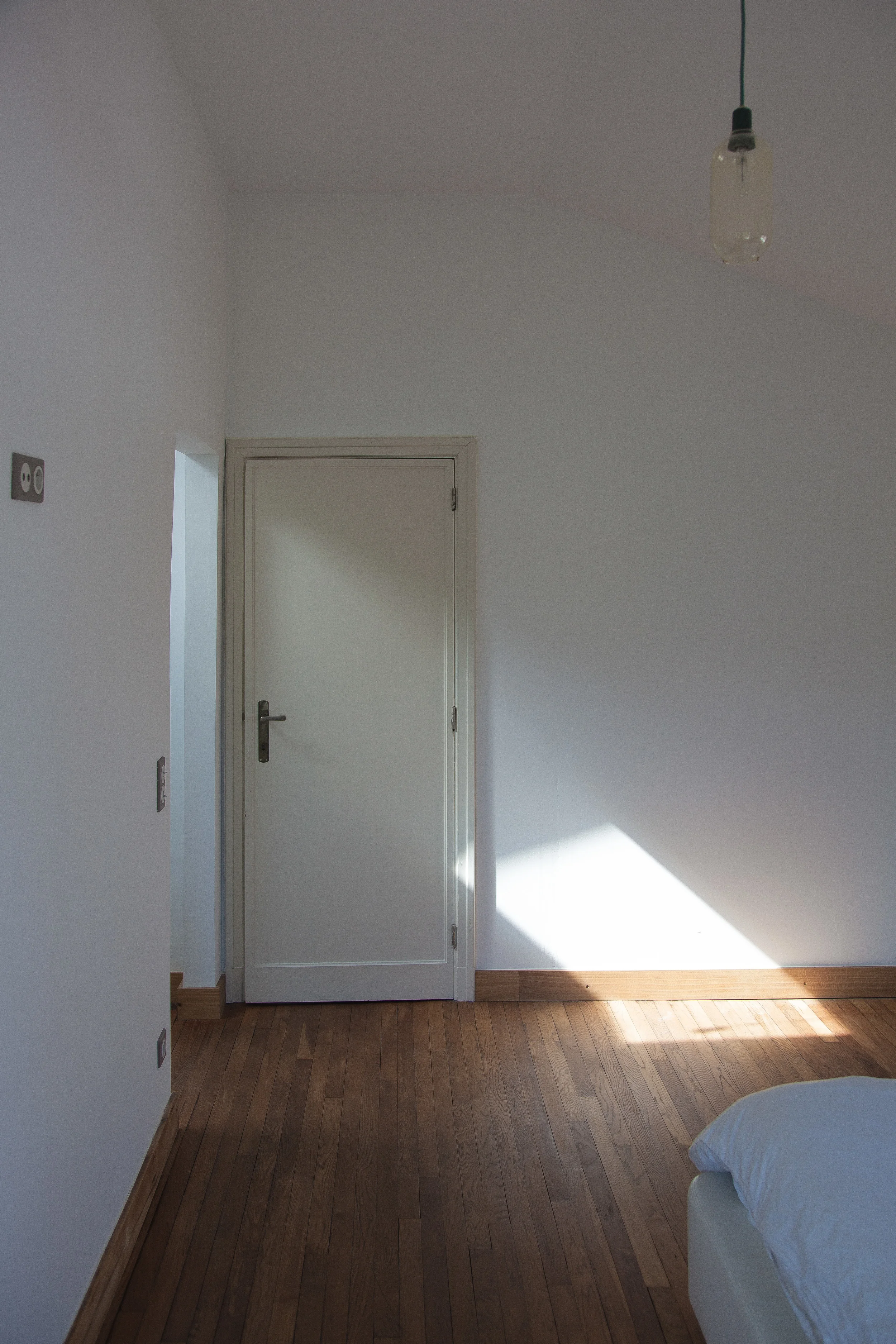 Minimalist residential bedroom interior featuring natural light, white walls, and warm wooden flooring.