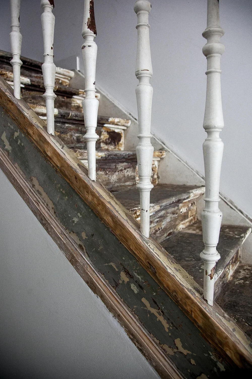 Old, worn wooden staircase with peeling paint and a white handrail with spindles.