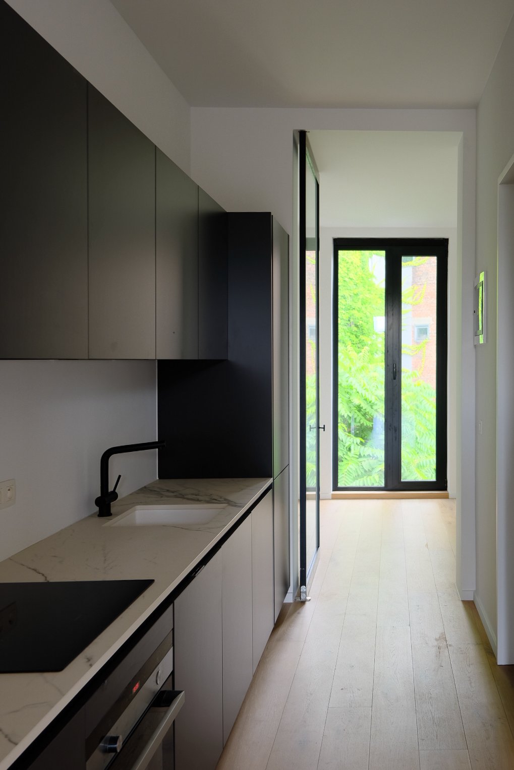 Bespoke modern kitchen with black upper cabinets, marble countertops, and large glass doors designed by Tom Naeyaert Architecture.