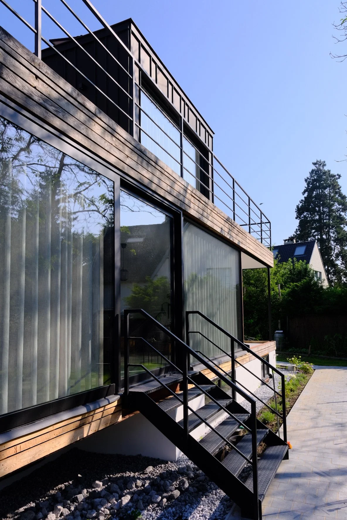 Contemporary residential architecture featuring a wooden exterior cladding and a custom metal staircase, designed by Tom Naeyaert Architecture.