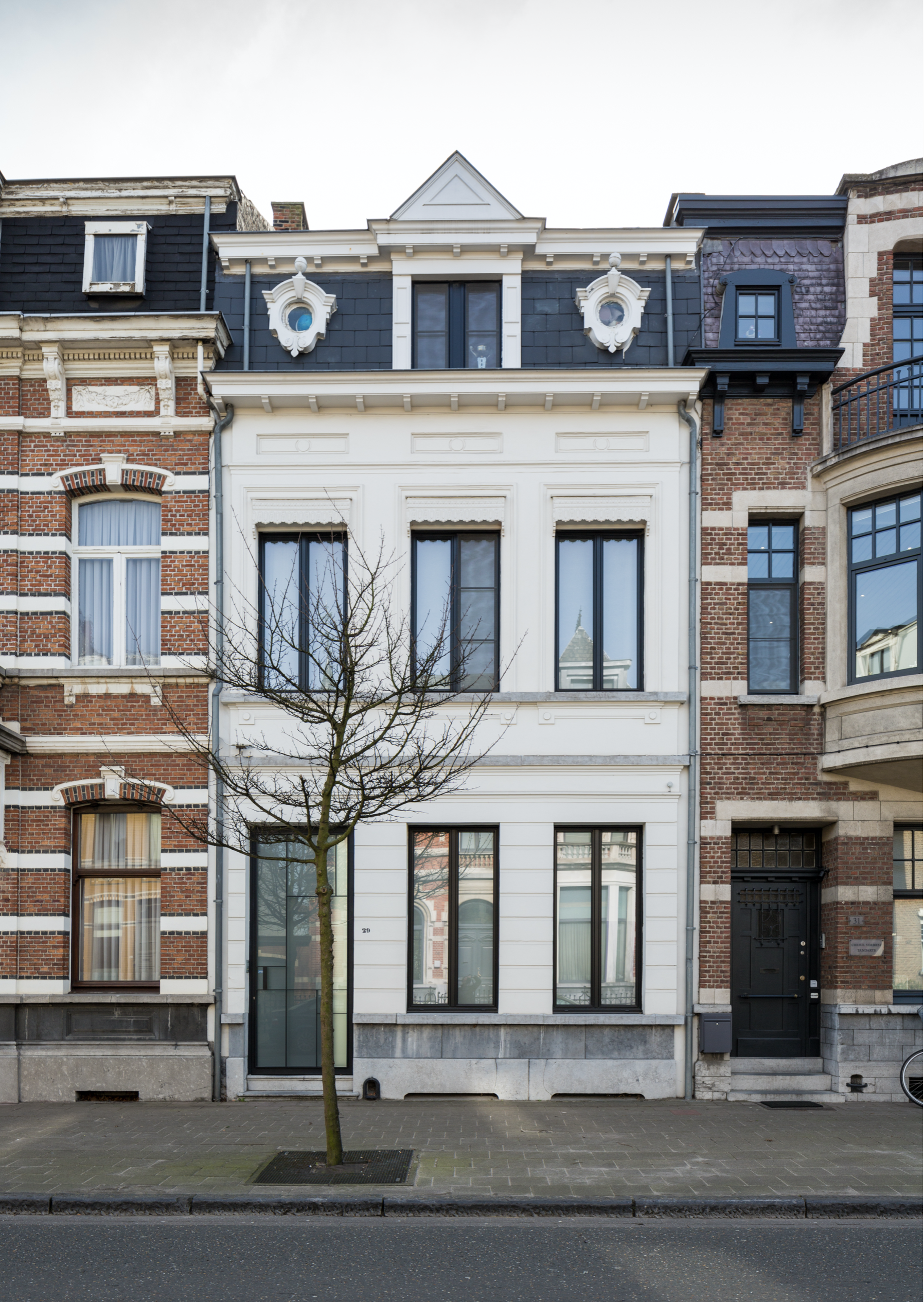 Contemporary townhouse renovation with a modern white facade and large black-framed windows, by Tom Naeyaert Architecture in Antwerp.