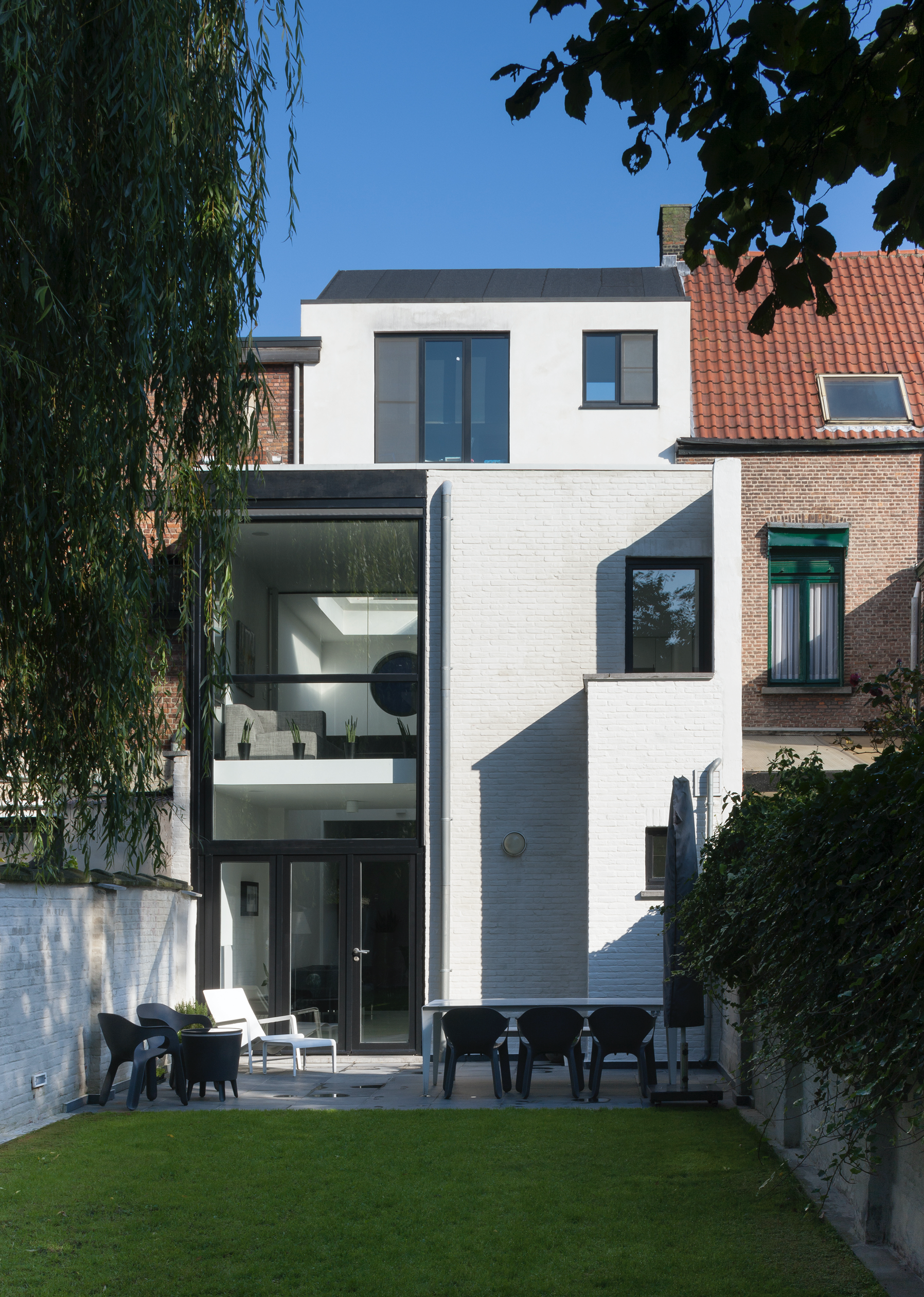 Modern residential architecture of a house with white brickwork, flat roof, and large black-framed windows, designed by Tom Naeyaert Architecture in Antwerp.