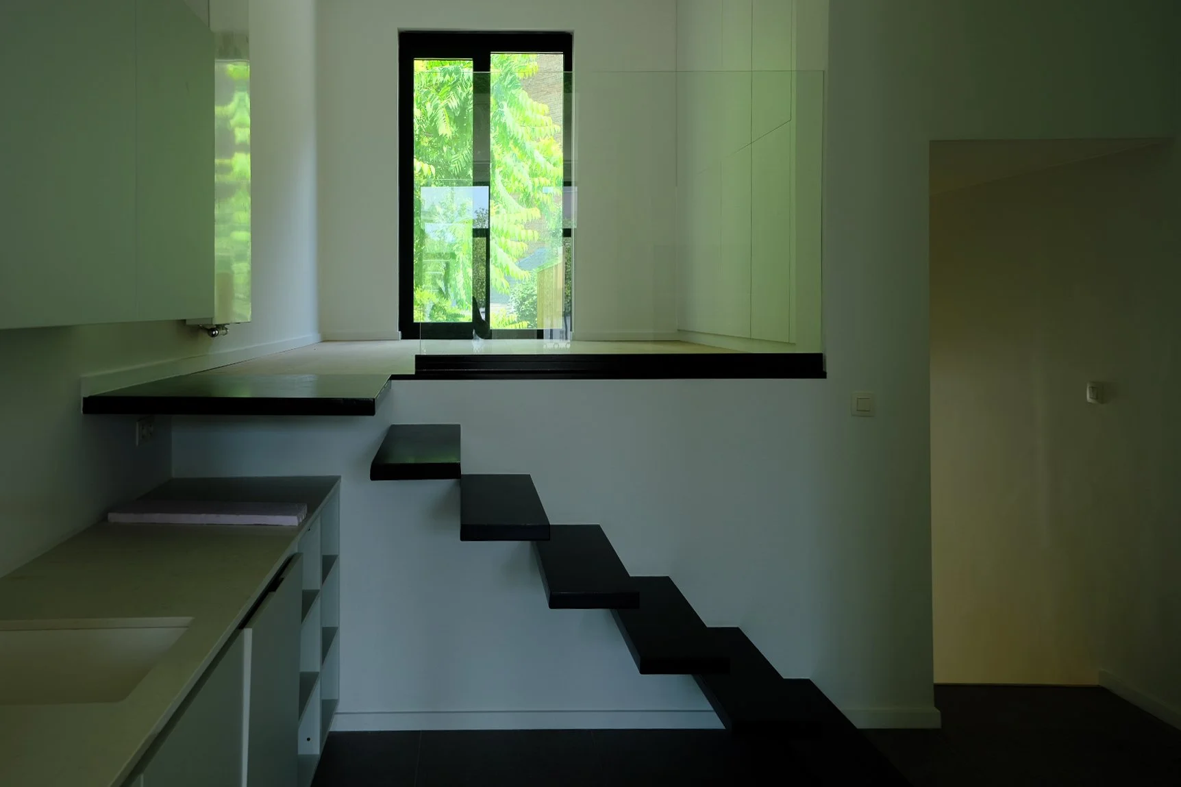 Minimalist residential interior with a modern black staircase and a large window overlooking greenery, crafted by Tom Naeyaert Architecture.