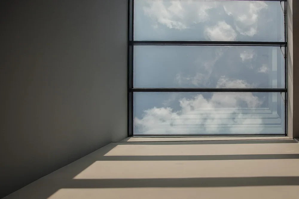 View of a glass window with clouds and sky outside, from inside a room with natural light.