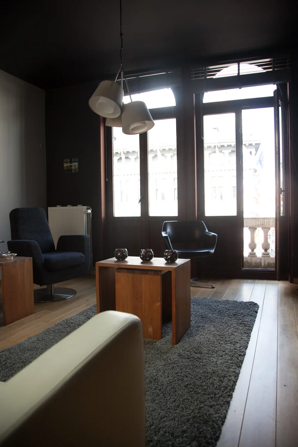 Contemporary residential living room interior featuring dark accent walls, large architectural windows, wooden flooring, and modern bespoke furniture, by Tom Naeyaert Architecture.