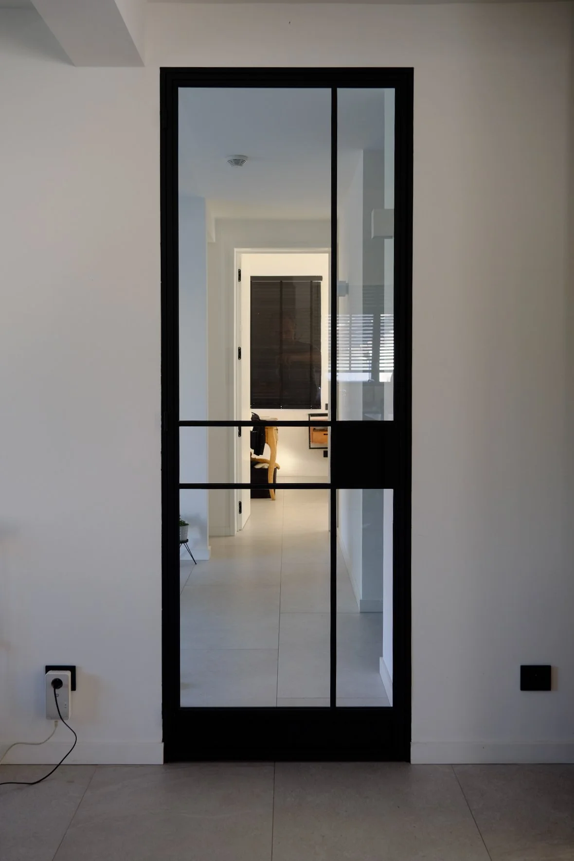 Architectural interior detail of a black-framed glass grid door leading into a tiled hallway, designed by Tom Naeyaert Architecture.