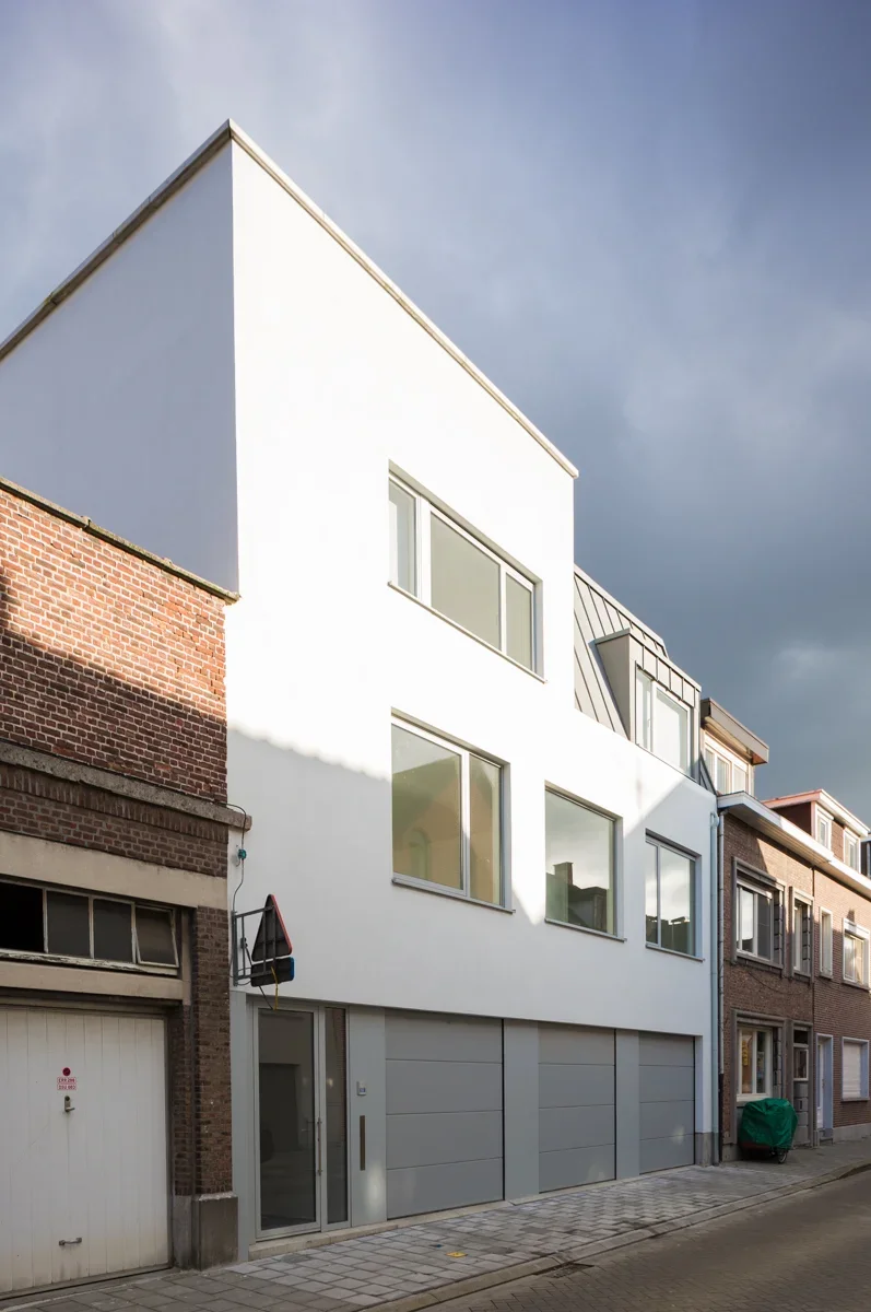 Modern white building with large windows next to older brick buildings under cloudy sky.
