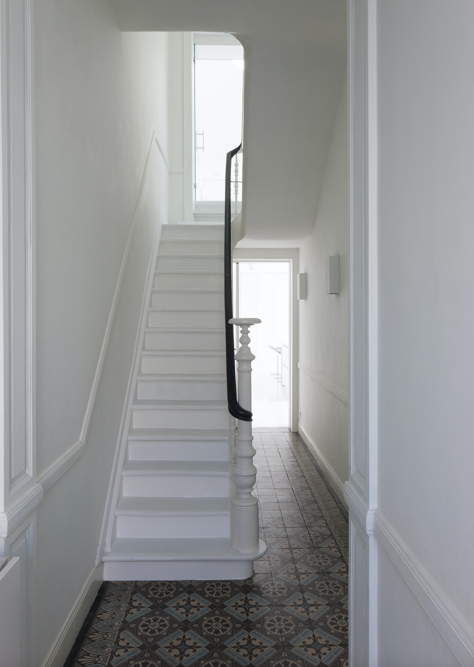 Interior architecture of a narrow hallway with patterned floor tiles and a minimalist staircase, designed by Tom Naeyaert Architecture in Antwerp.
