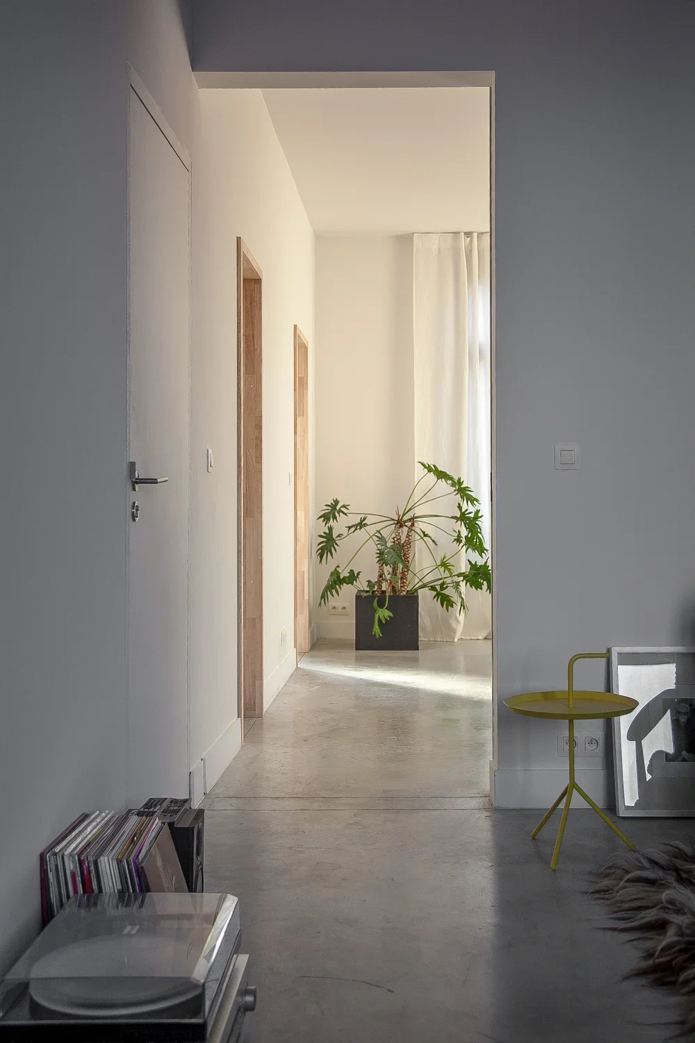 Interior view of a modern apartment hallway with a potted plant near a window, a yellow side table, vinyl records, and a turntable.