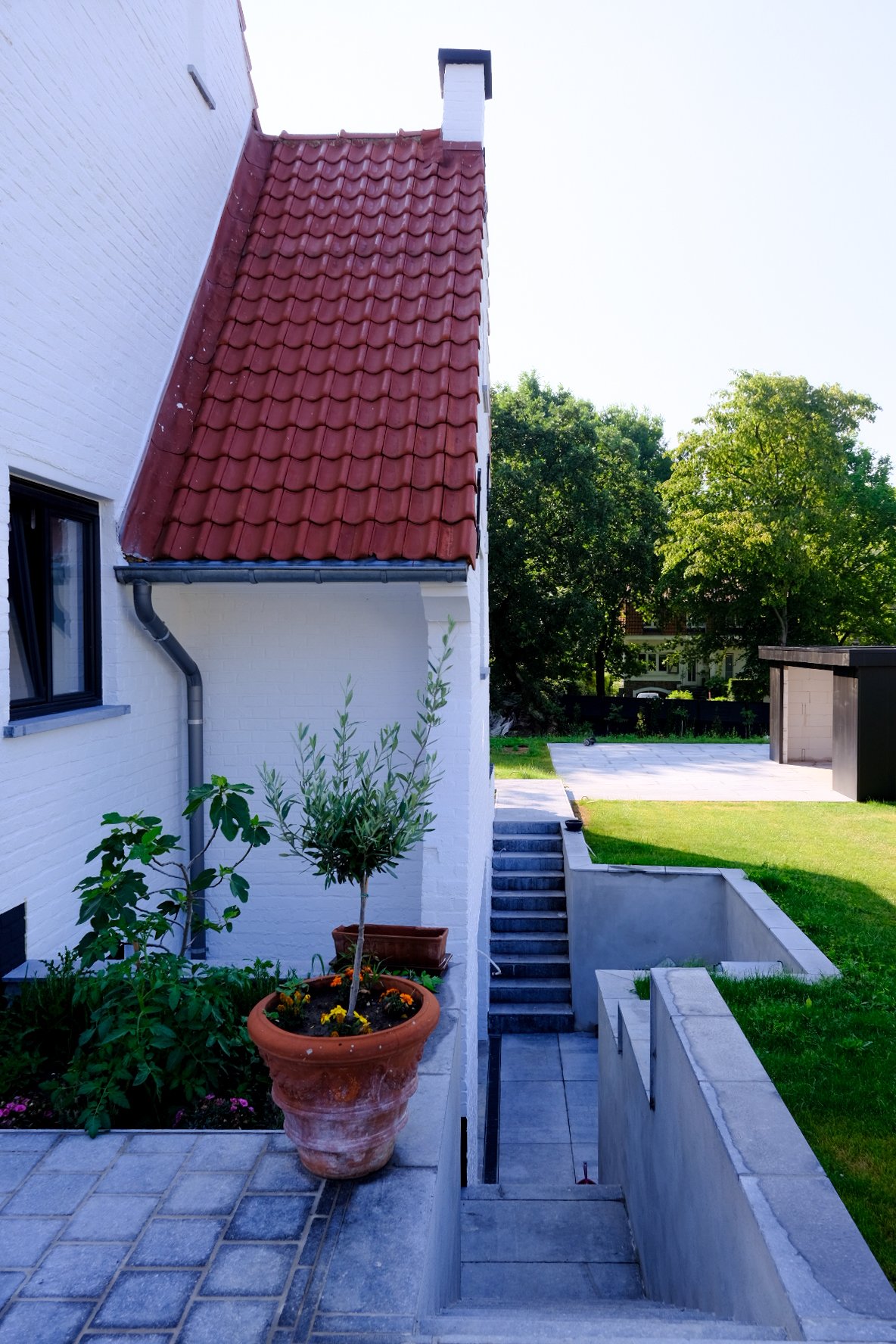 Exterior view of a modern residential house with a white brick facade and architectural landscaping, designed by Tom Naeyaert Architecture in Antwerp.