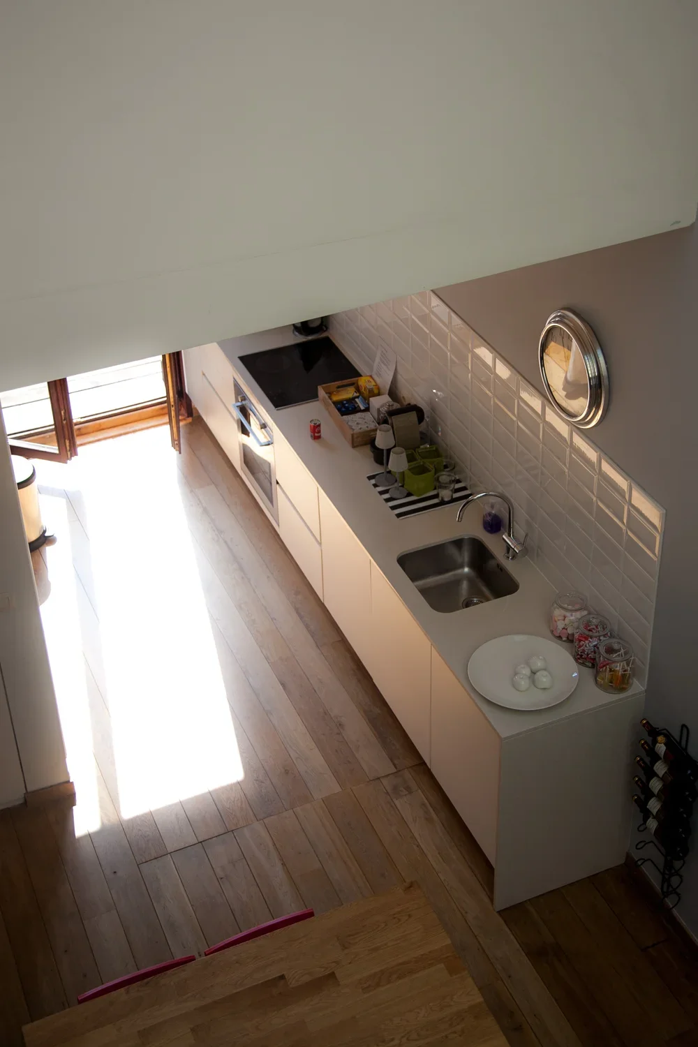 Overhead perspective of a contemporary kitchen design featuring sleek white cabinets, wooden flooring, integrated appliances, and natural light streaming through glass doors, by Tom Naeyaert Architecture.