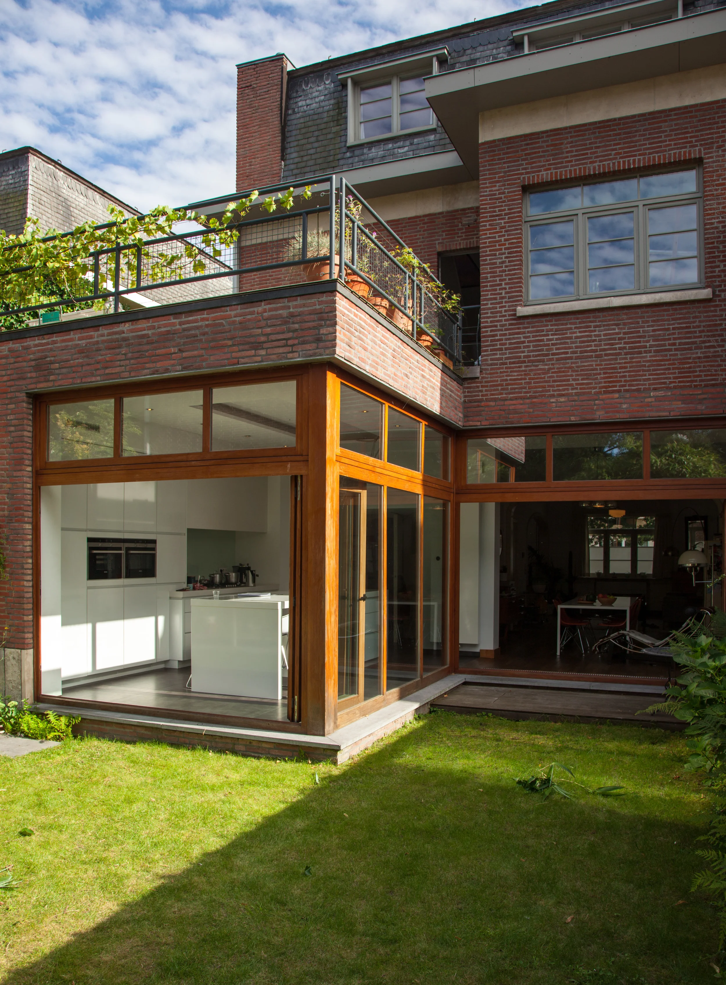 Contemporary residential architecture with a classic brick exterior, featuring a custom wooden-framed sunroom and integrated balcony.