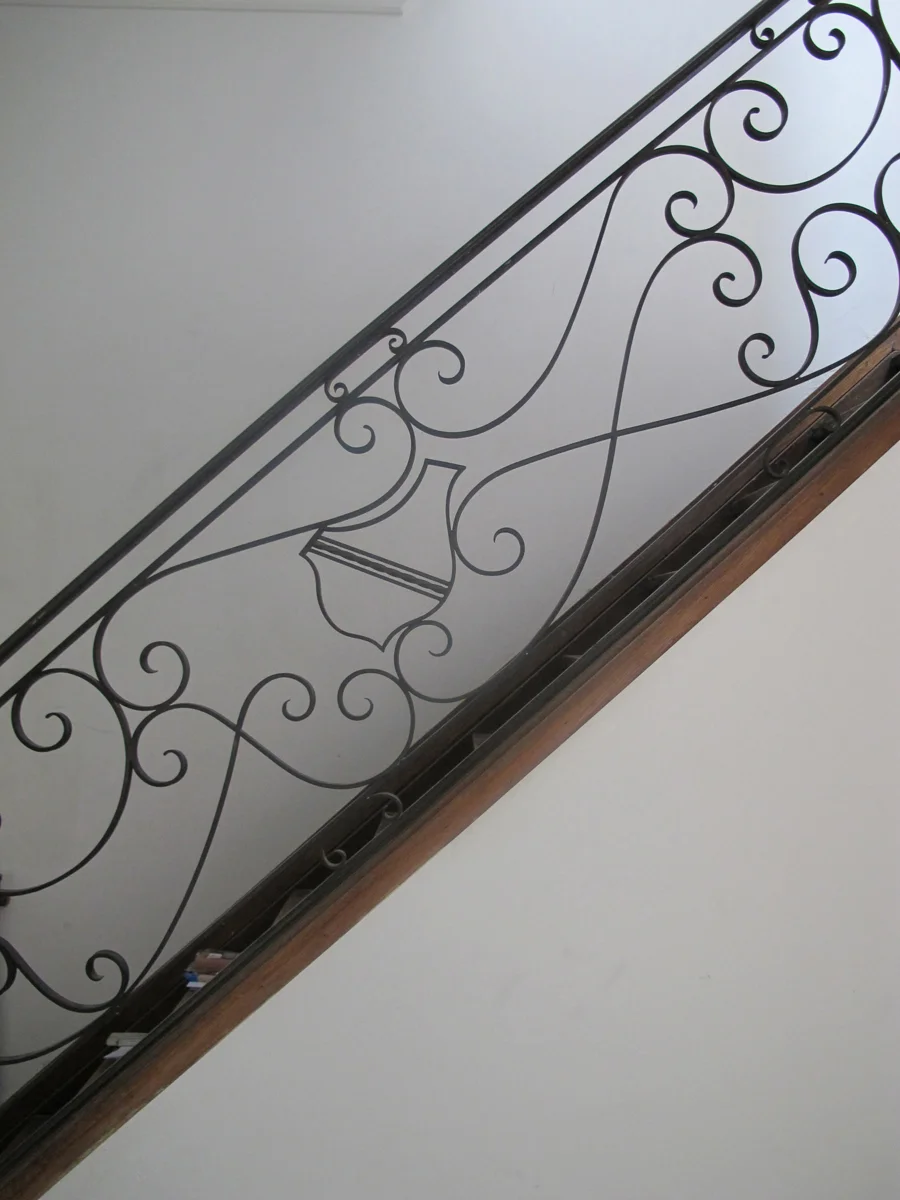 Decorative staircase railing with ornate black iron scrollwork and a wooden handrail.