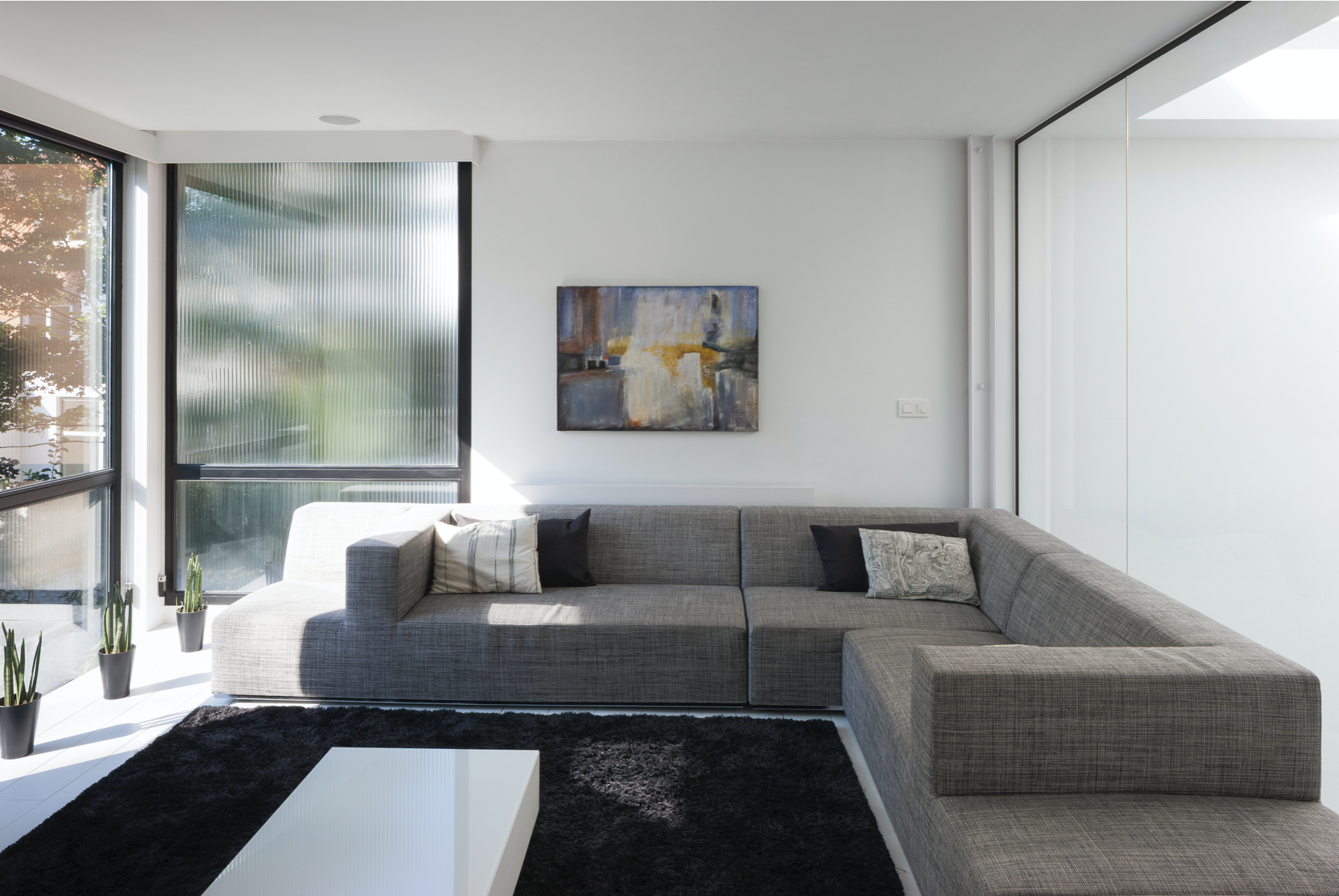 High-end contemporary living room interior design featuring floor-to-ceiling windows and a large sectional sofa, by Tom Naeyaert Architecture.