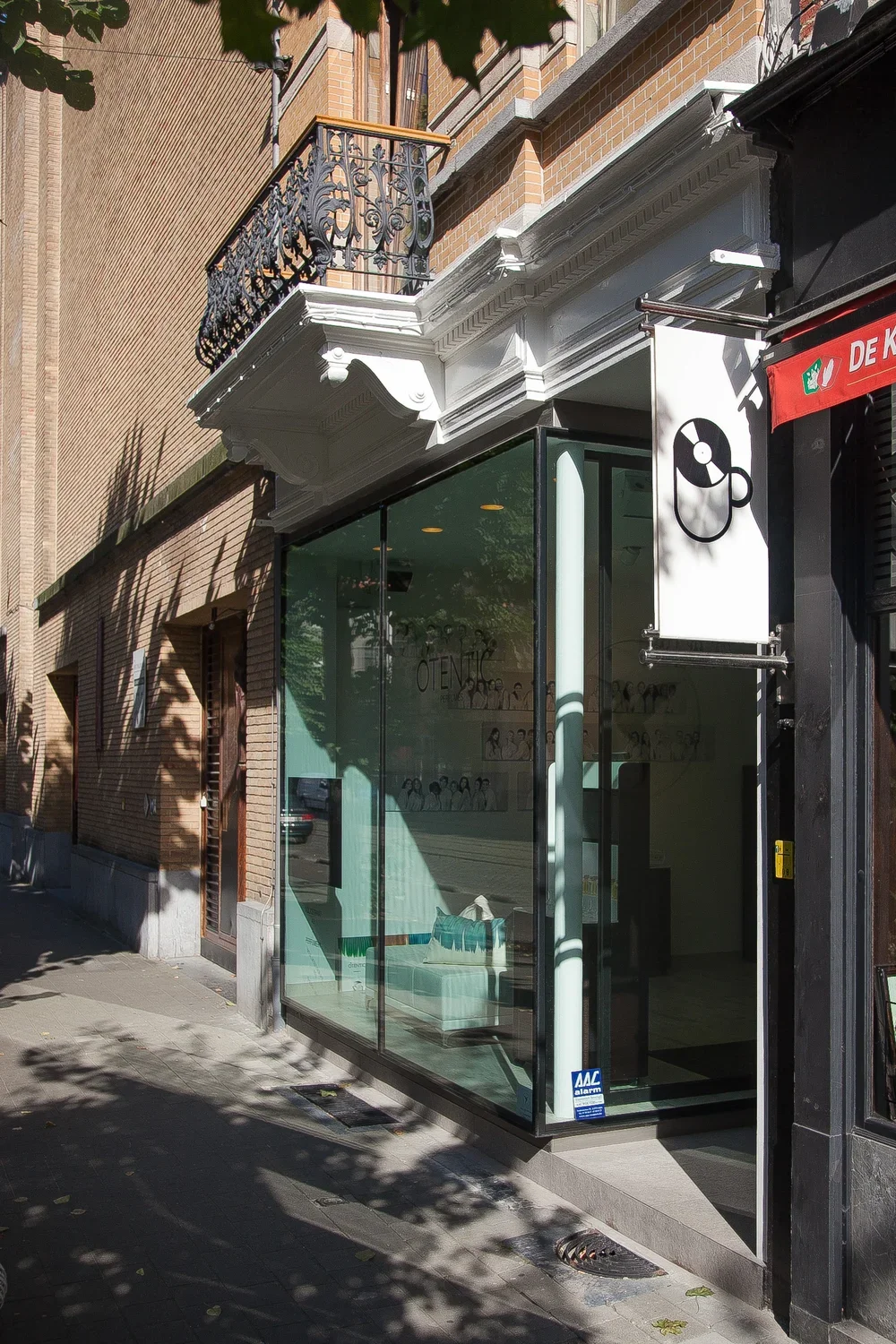 storefront with large glass windows, white ornate cornice, black wrought iron balcony, and a sign with a coffee cup and CD icon outside.