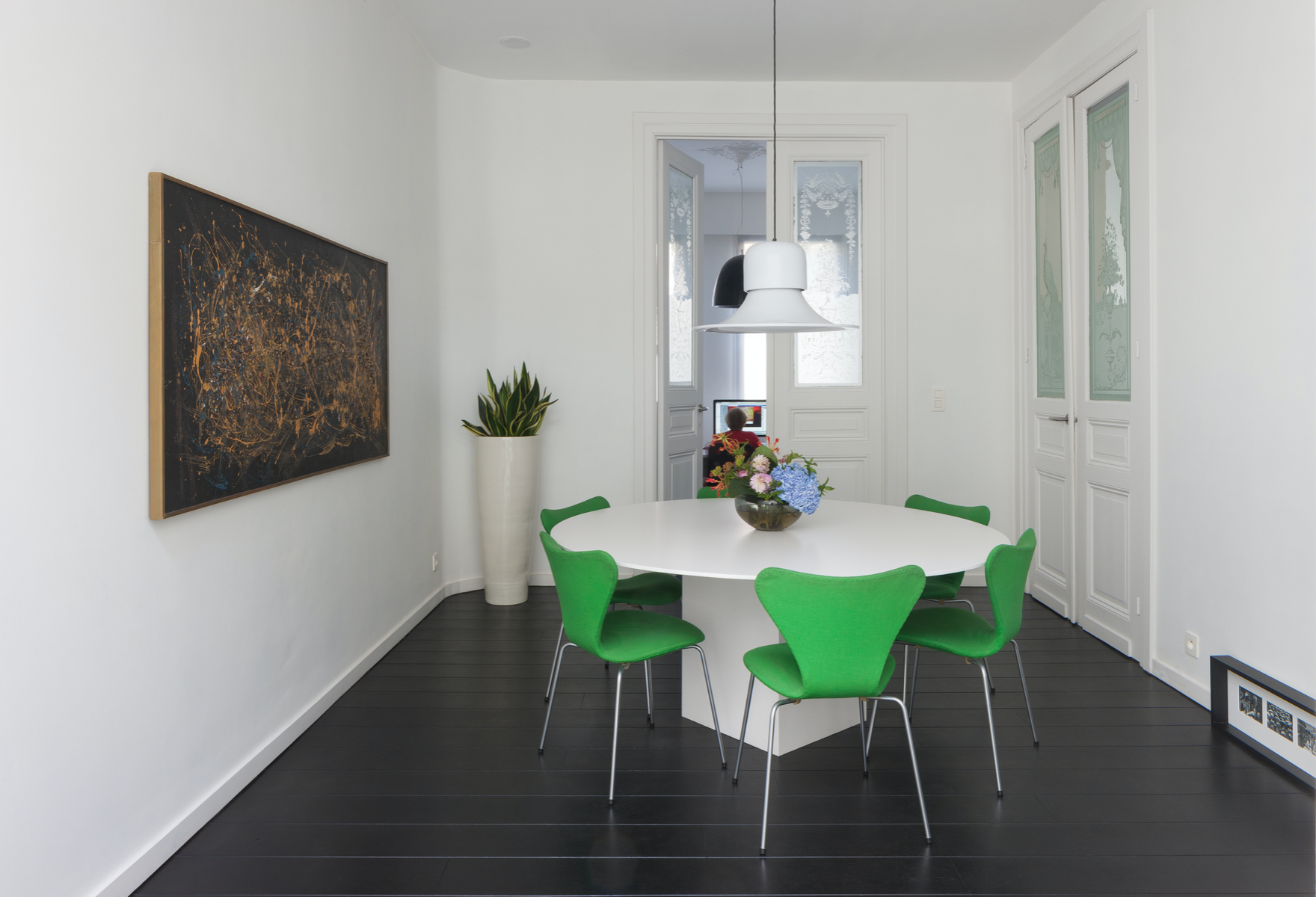 Modern residential dining room interior design featuring a white round table, green chairs, and bespoke layout by Tom Naeyaert Architecture.