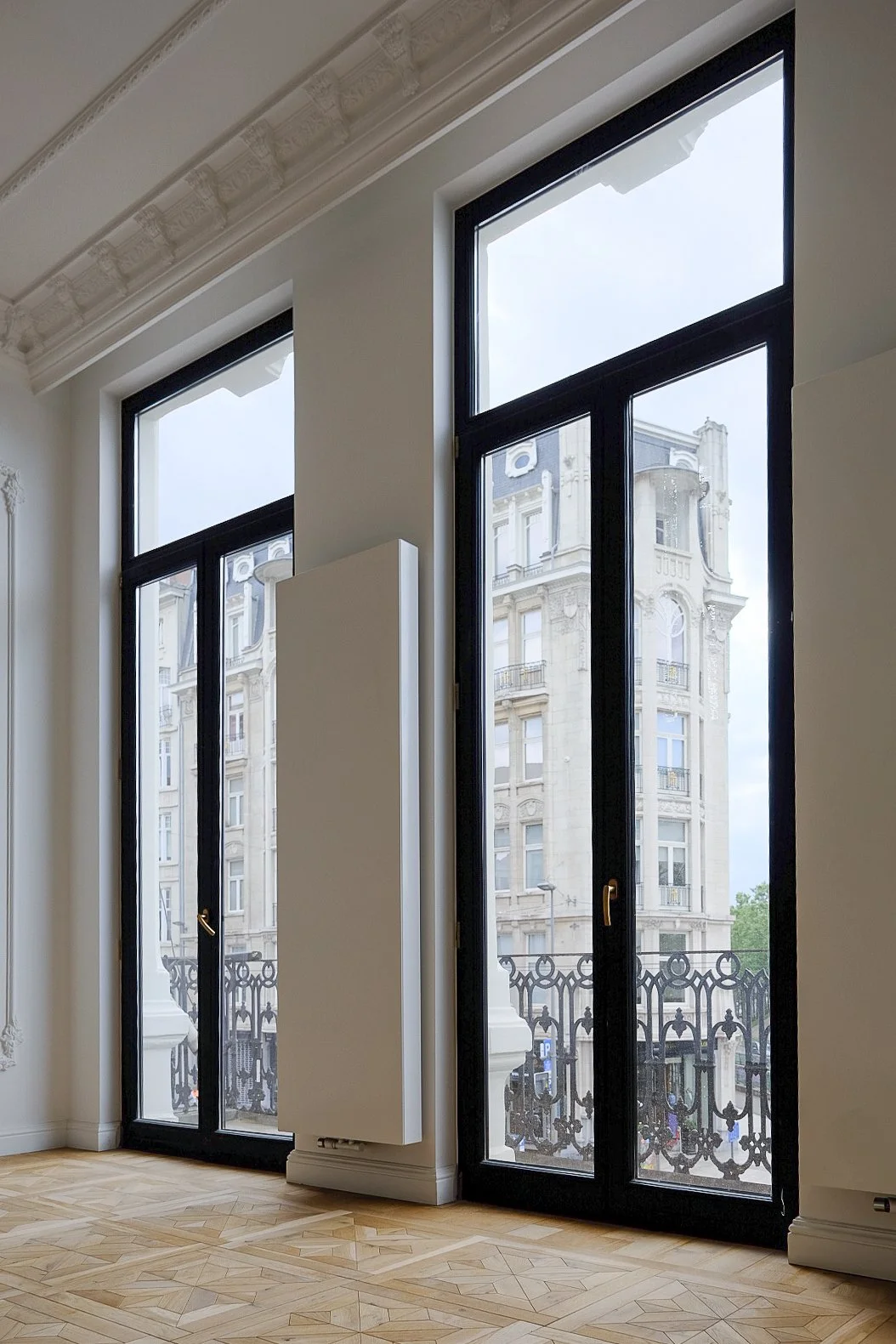 Historic townhouse renovation featuring large black-framed windows and ornate trim, designed by Tom Naeyaert Architecture in Antwerp.