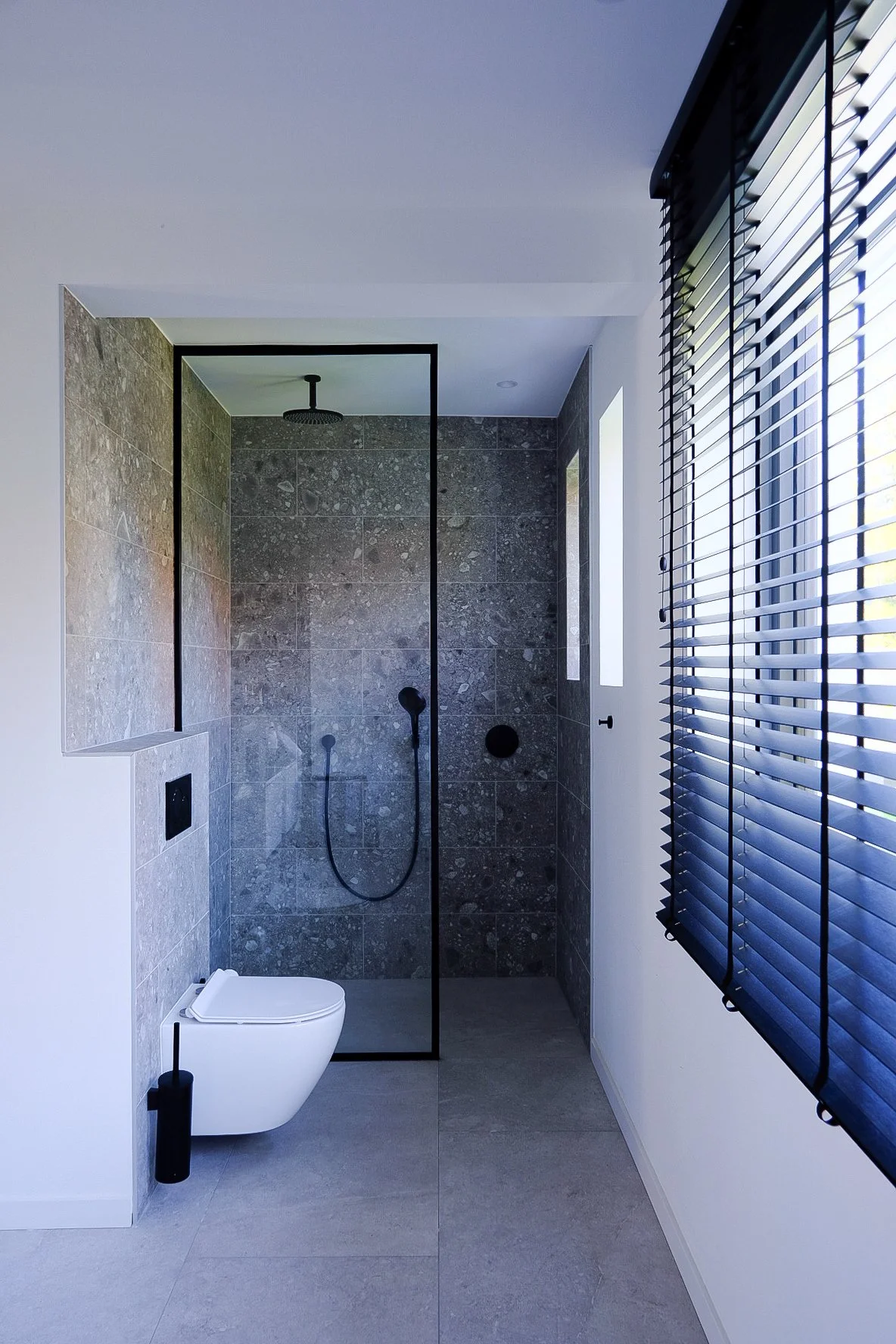 Modern bathroom interior design with a walk-in shower featuring gray stone tiles and black fixtures, by Tom Naeyaert Architecture.