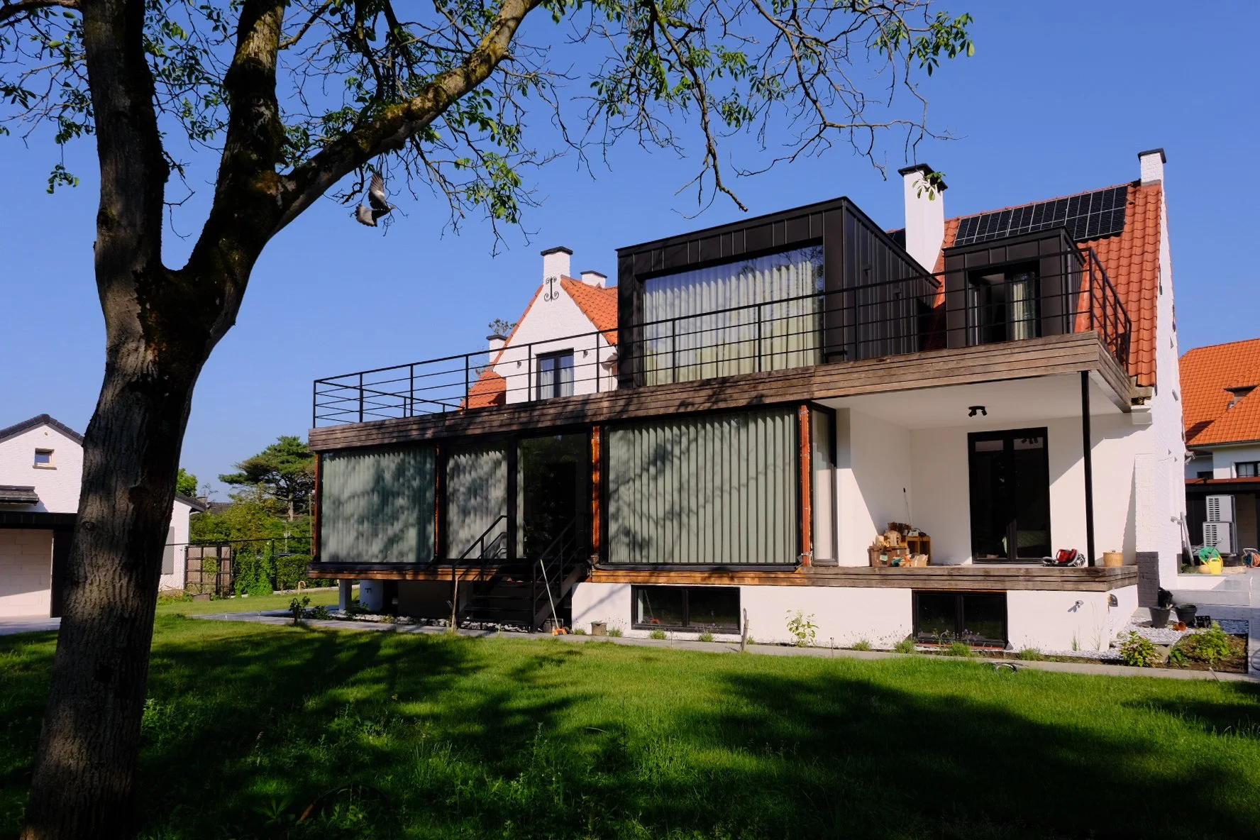 Modern two-story residential house renovation with white walls, a traditional red tiled roof, and large glass windows, by Tom Naeyaert Architecture in Antwerp.