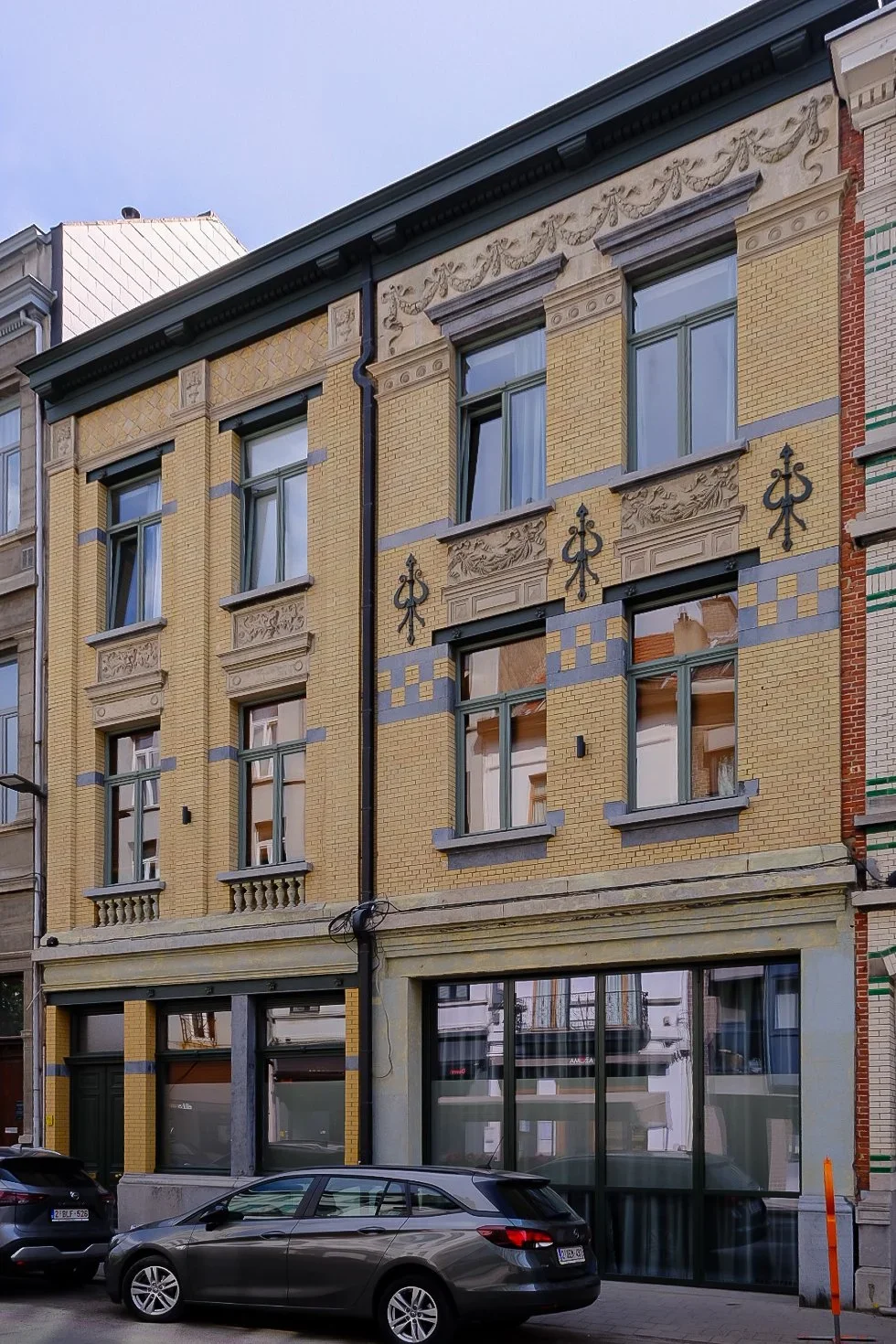 Three-story residential building design featuring a yellow brick facade, large ground-floor windows, and decorative stone accents, by Tom Naeyaert Architecture.
