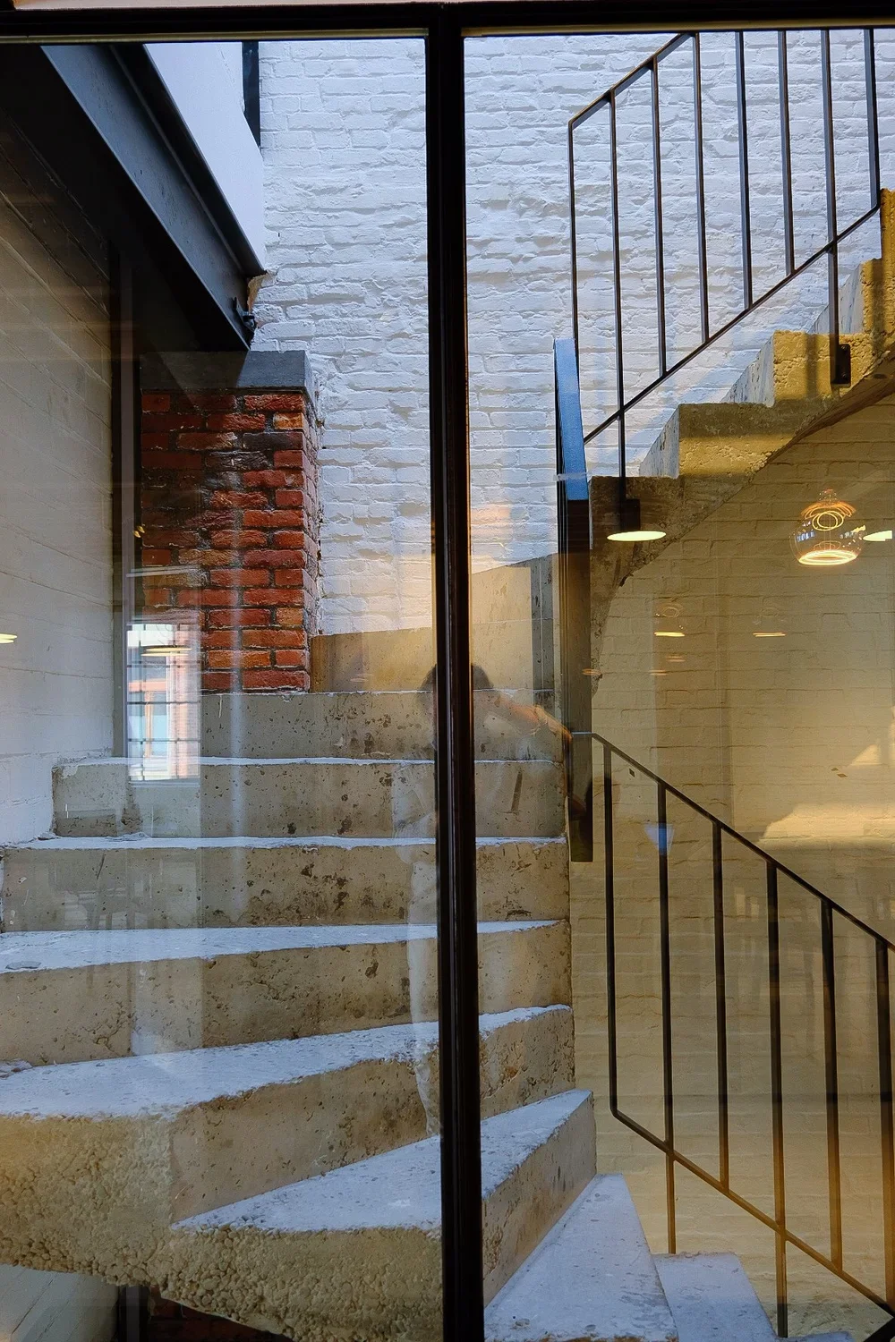 Modern concrete staircase with minimalist metal railing inside a contemporary building, viewed through architectural glass, by Tom Naeyaert Architecture.