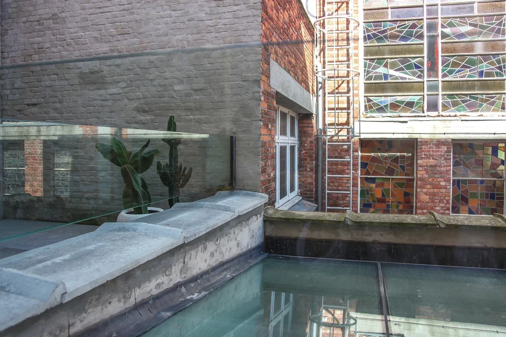 Urban courtyard with a glass railing, potted cactus plants, a brick wall, and a stained glass window.