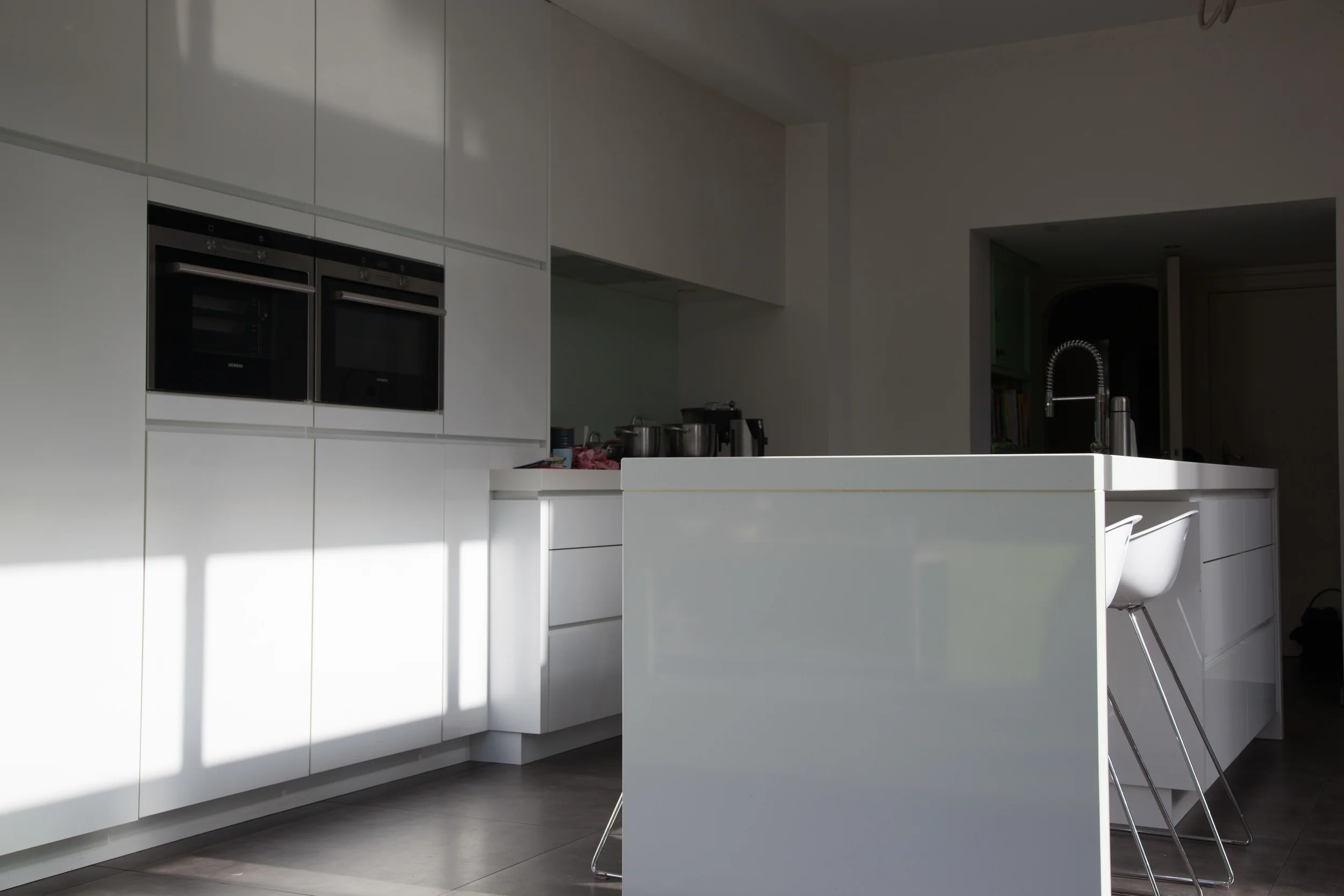 Modern kitchen with white cabinetry, built-in ovens, and a white island with a barstool.