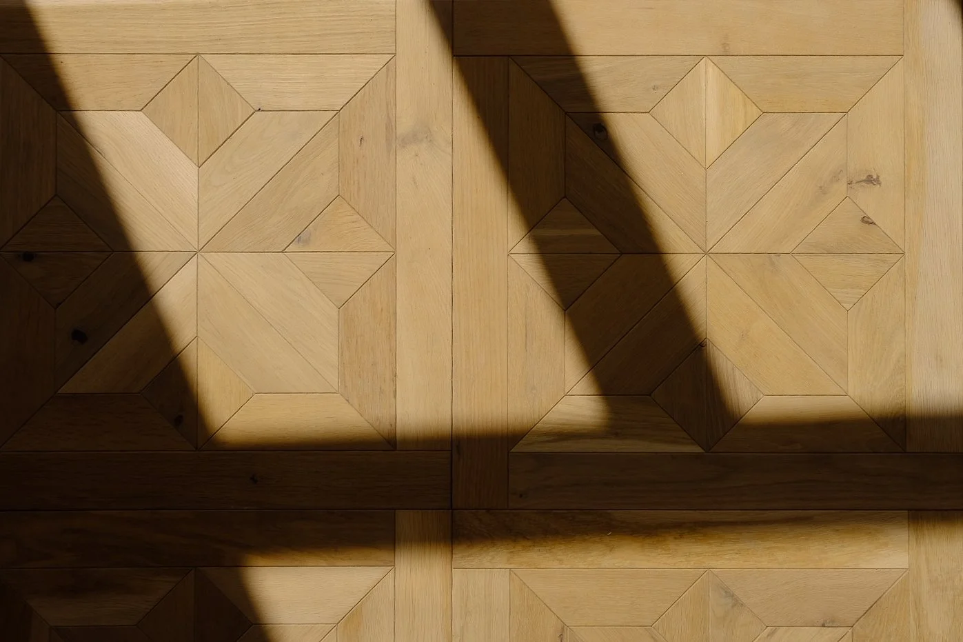 Close-up detail of a wooden parquet floor with intricate geometric patterns, part of a bespoke interior design project by Tom Naeyaert Architecture.