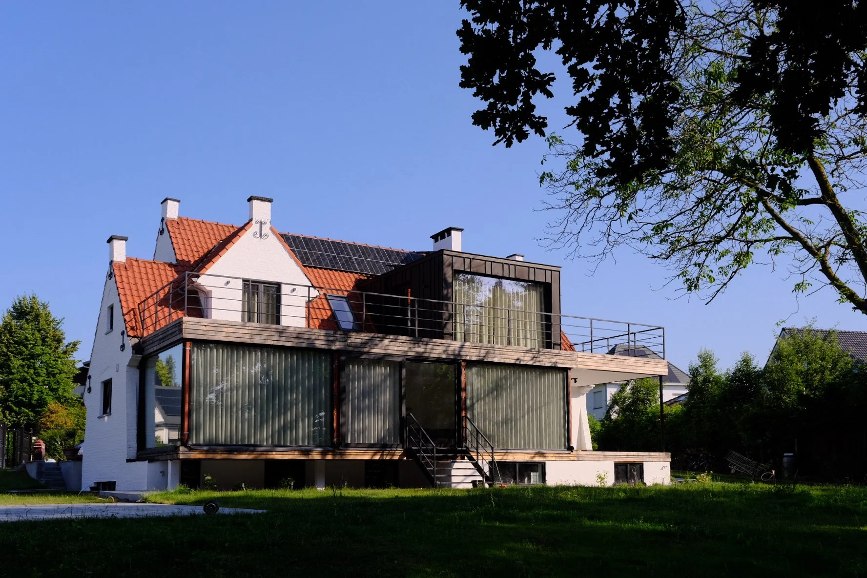 Modern residential house architecture with white walls and a large glass balcony, designed by Tom Naeyaert Architecture.