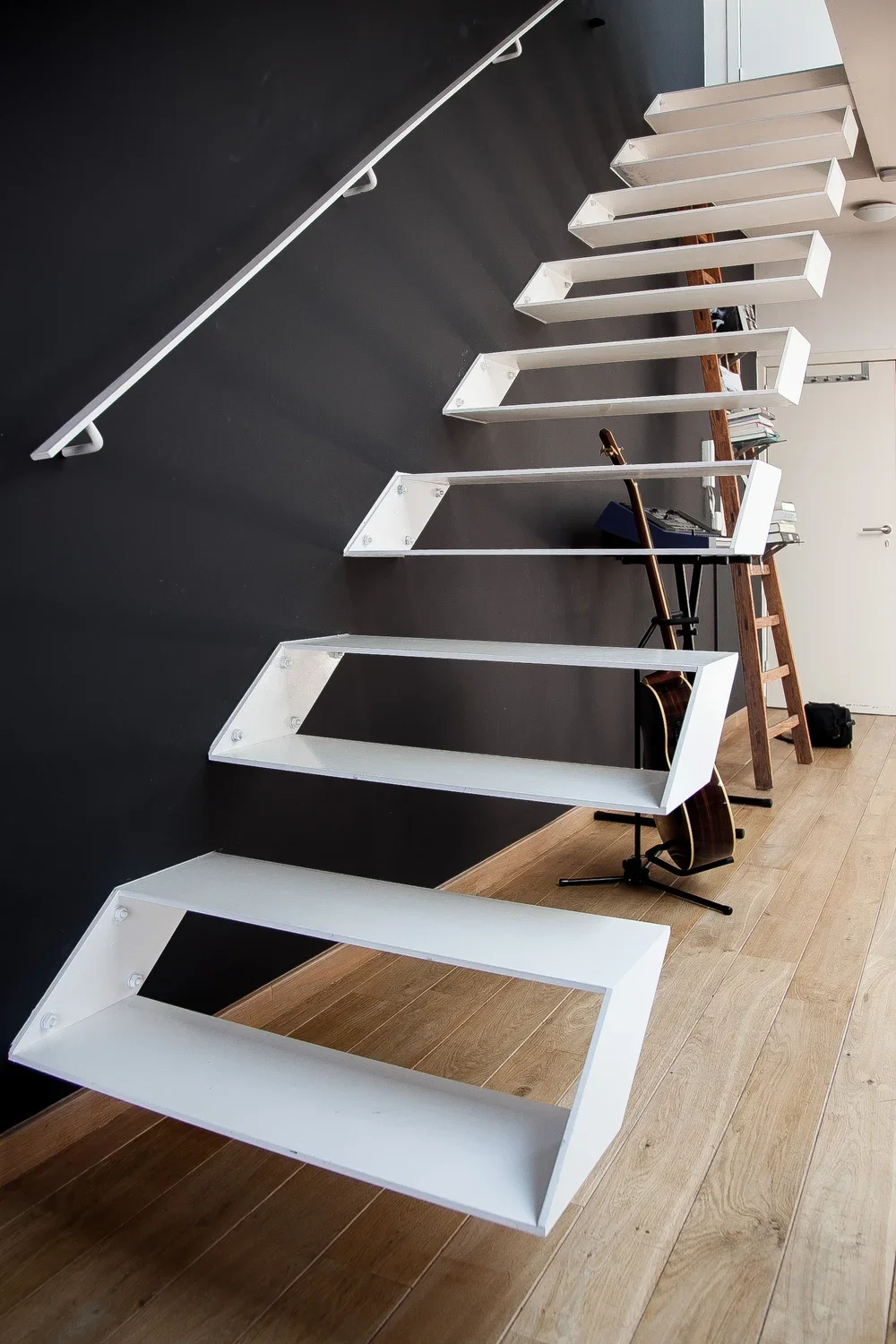 Custom white floating shelves mounted on a minimalist black feature wall, highlighting modern interior architecture and bespoke storage solutions, by Tom Naeyaert Architecture.