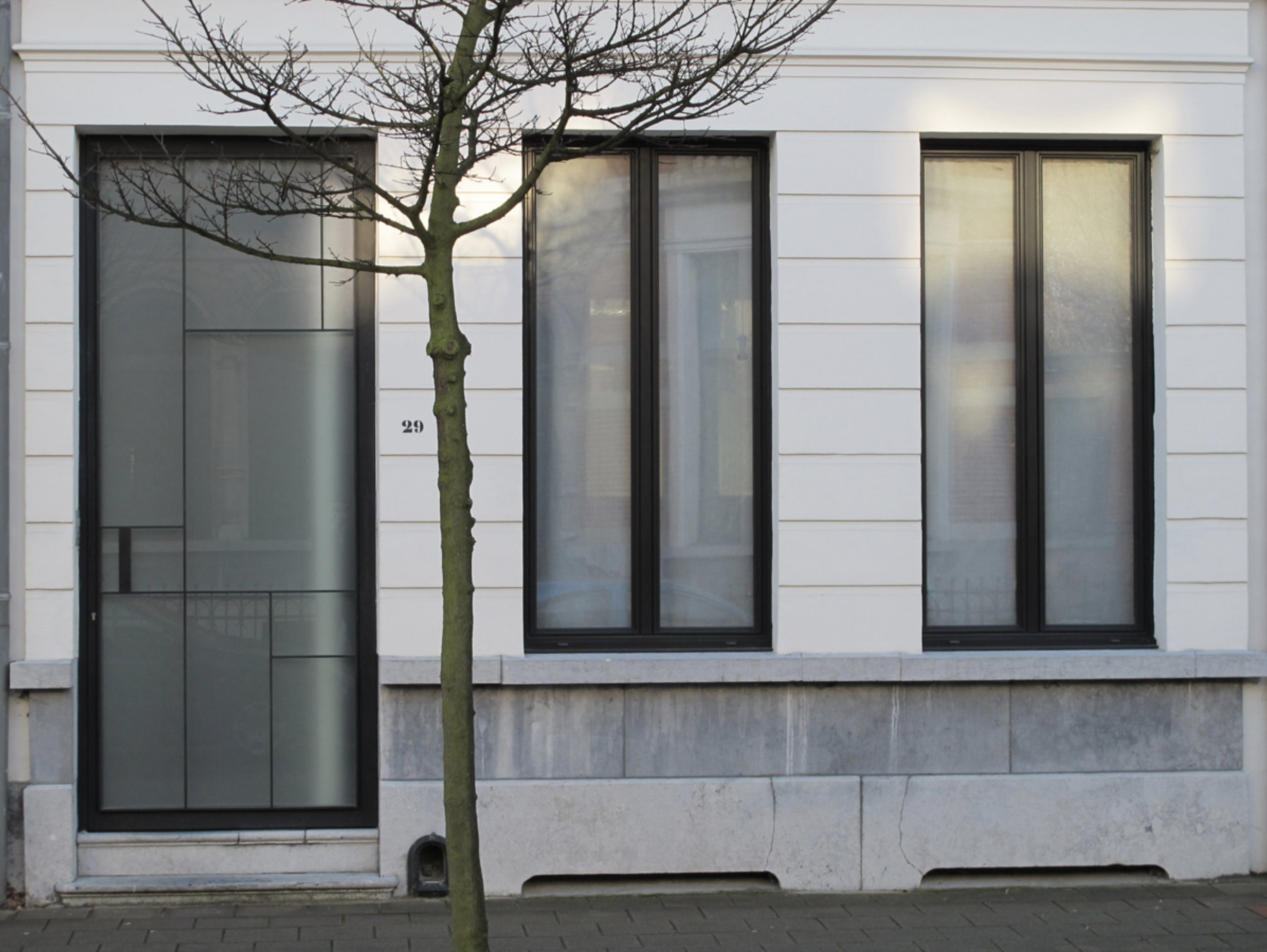 Modern white residential building facade with large black-framed windows, designed by Tom Naeyaert Architecture, Antwerp.