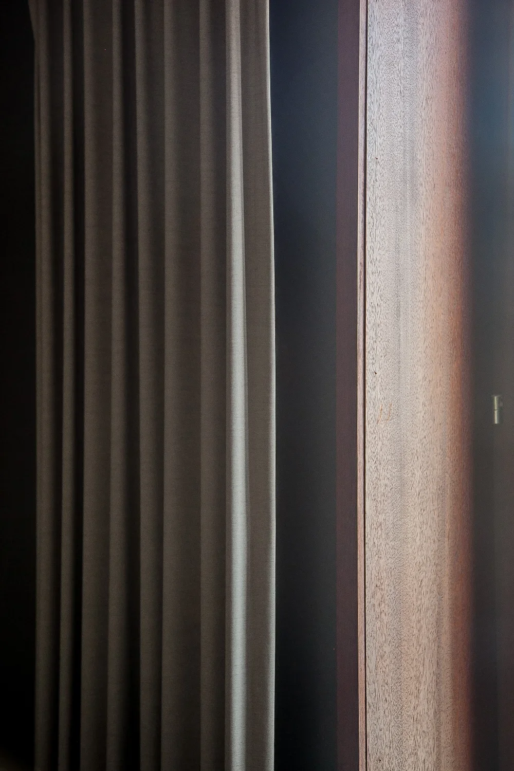 Close-up architectural detail of a premium wooden door and custom minimalist curtains, showcasing refined residential interior design, by Tom Naeyaert Architecture.