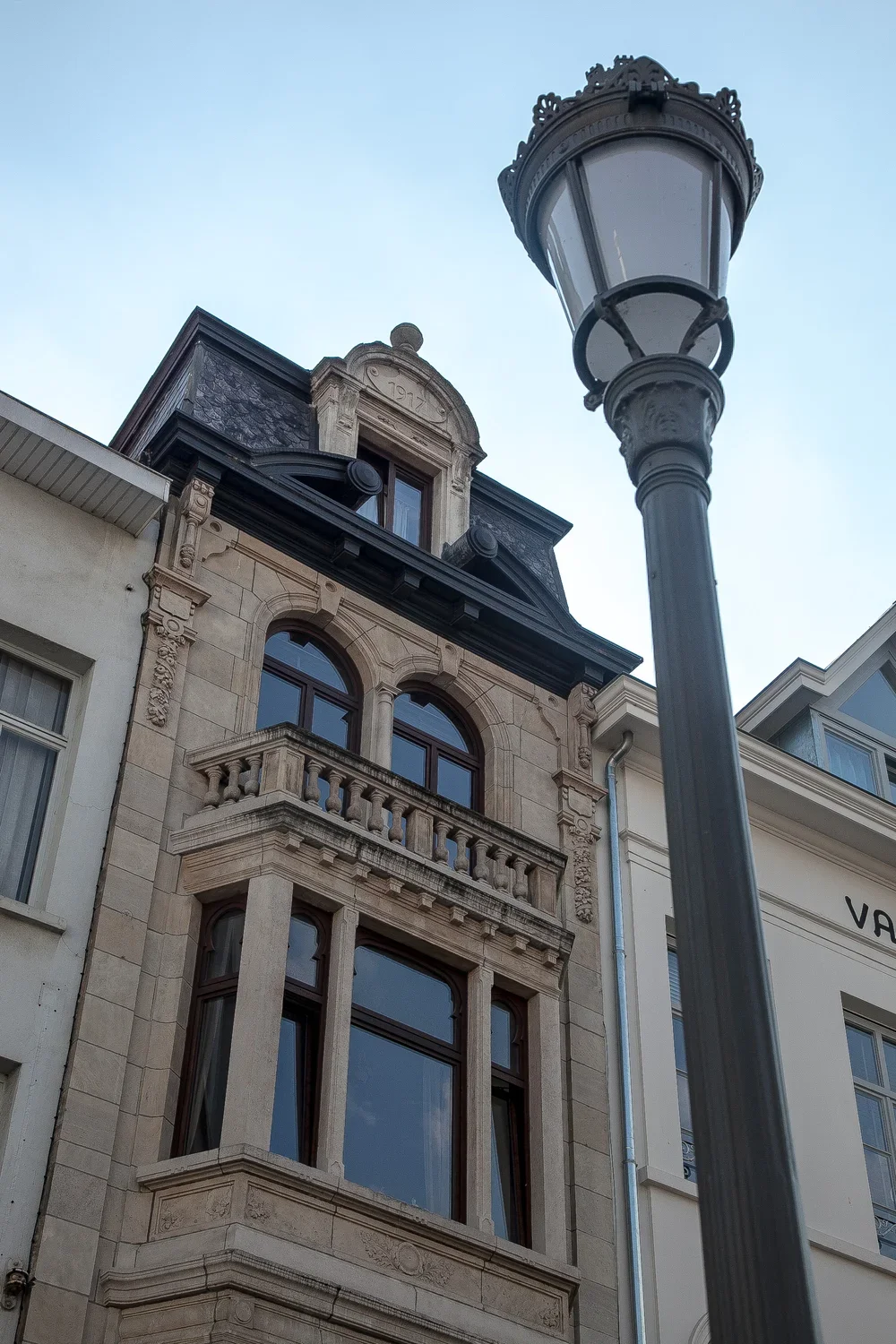 Historic building restoration with intricate architecture and arched windows, framed by a classic street lamp in Antwerp, by Tom Naeyaert Architecture.