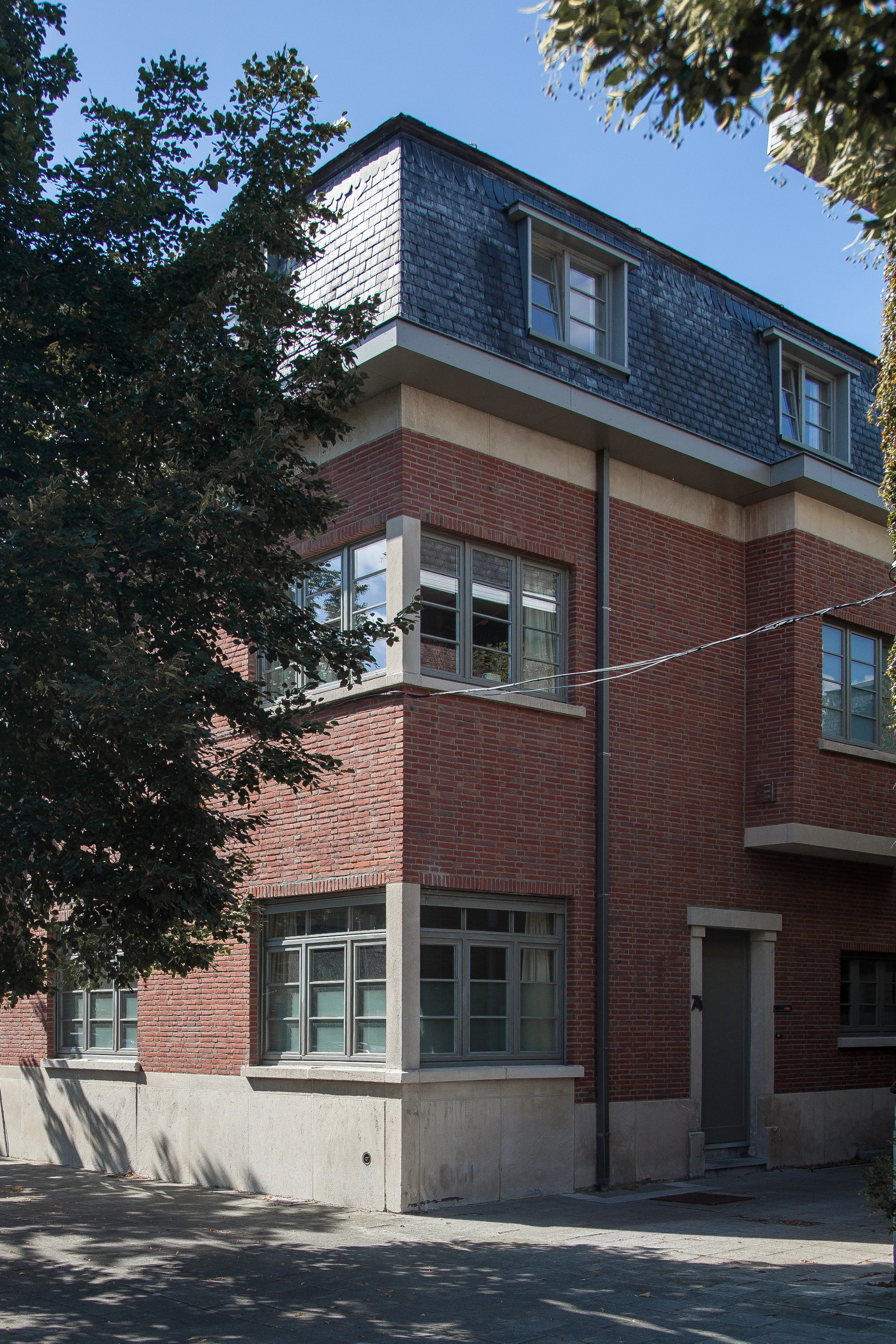 Modern multi-story residential building featuring a traditional brick facade, expansive windows, and a slate roof design.